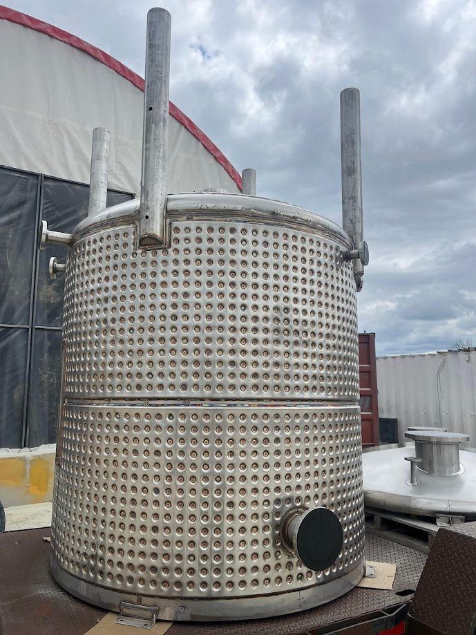 A large stainless steel tank is sitting on top of a table in front of a building.