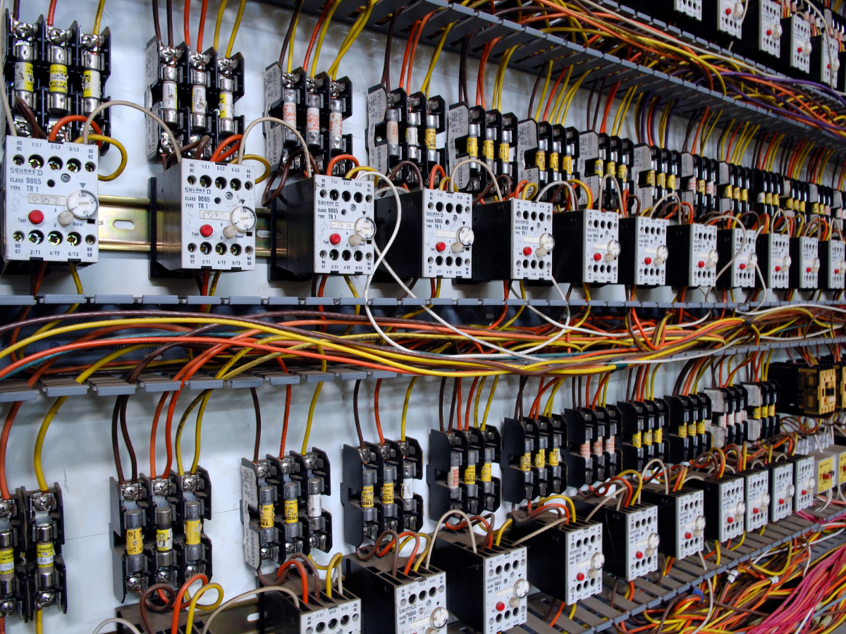 Electrical control panel with rows of relays, switches, and wiring in various colors.