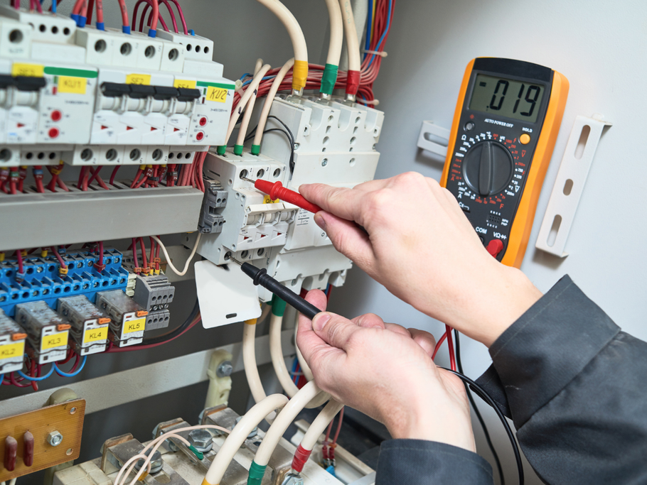Electrician using a multimeter to test wiring in a circuit breaker panel.