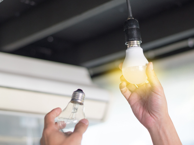 Person replacing lightbulb in a fixture, holding old bulb and new LED bulb.