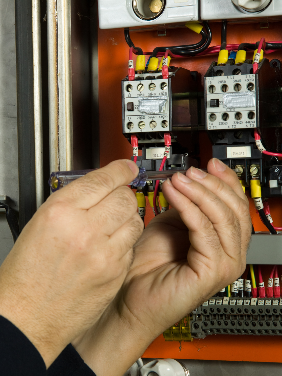 Hands working on electrical wiring in an industrial control panel.
