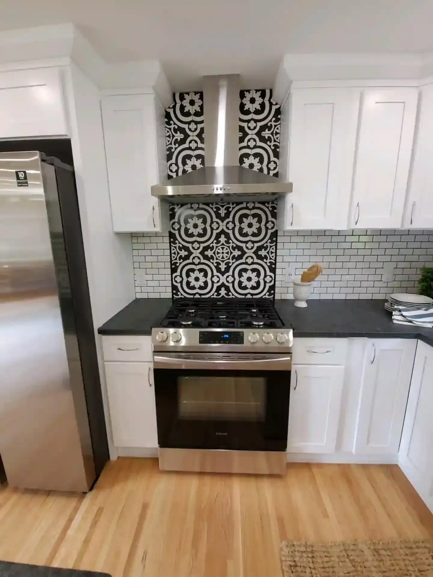White kitchen with stainless steel appliances, black countertops, and patterned backsplash.