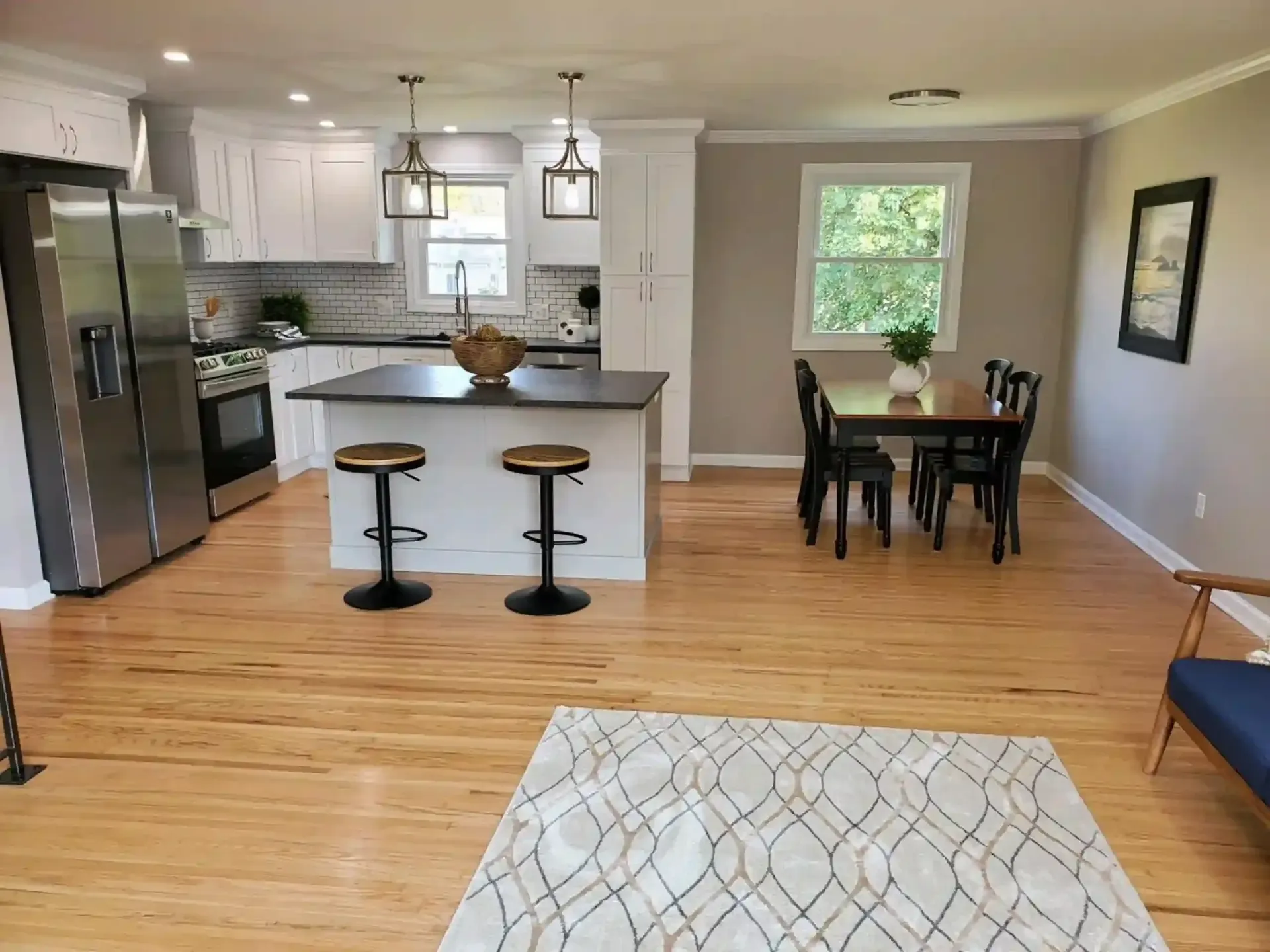 Open-concept kitchen and dining area with white cabinets, dark island, wood floors, and black dining table.