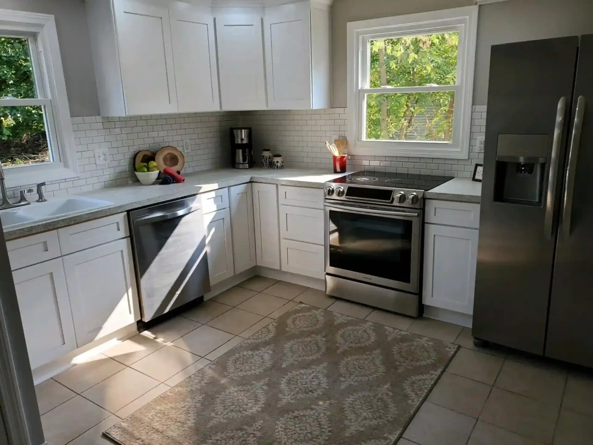 White kitchen with cabinets, appliances, tile backsplash, and rug.