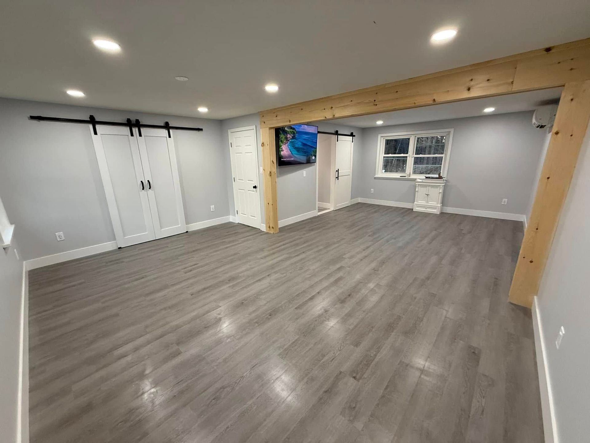 Empty, modern basement with light gray walls, wooden beam, and gray flooring. Includes two sliding barn doors.