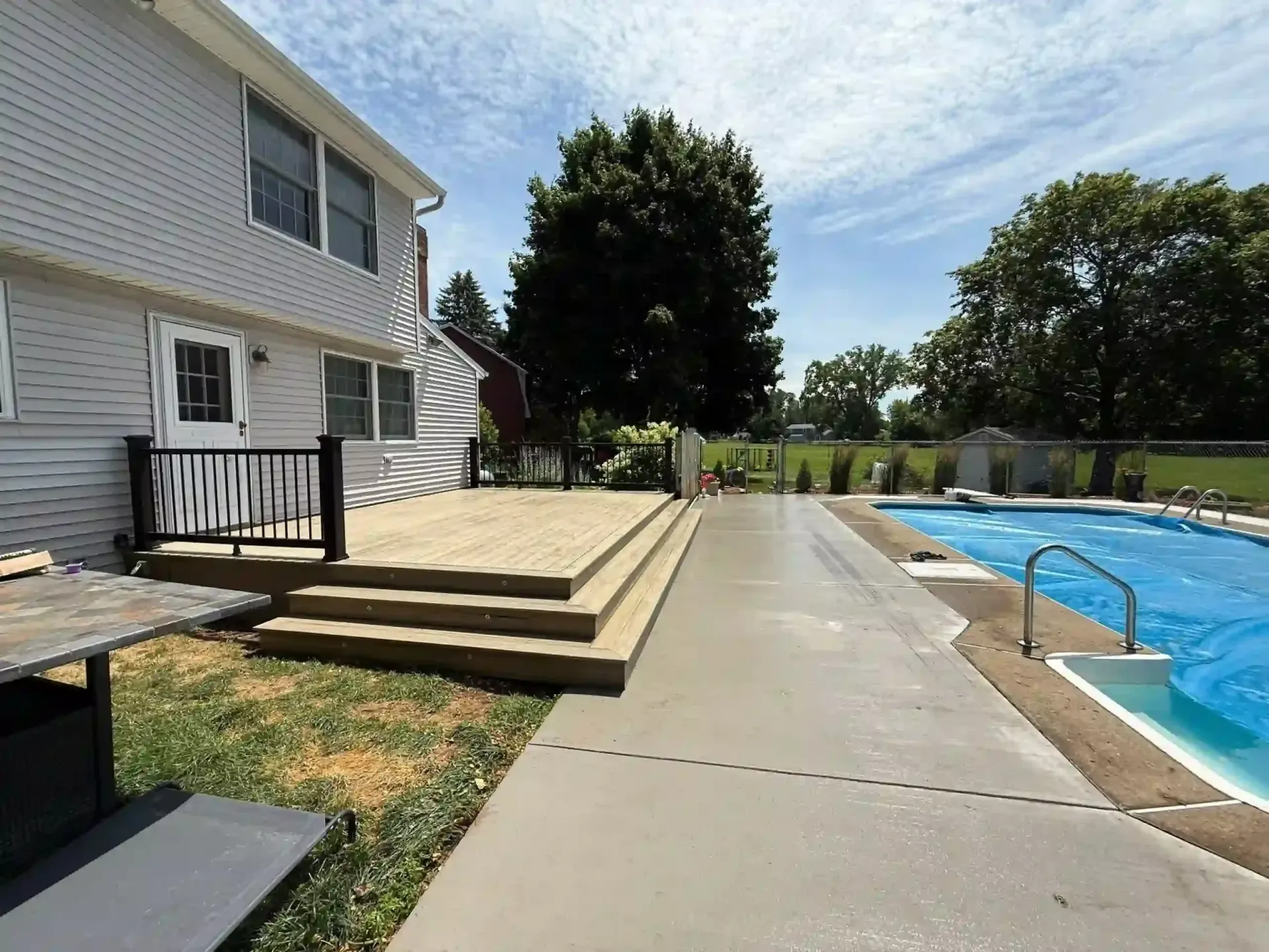 Backyard with a deck, pool, and house on a sunny day.