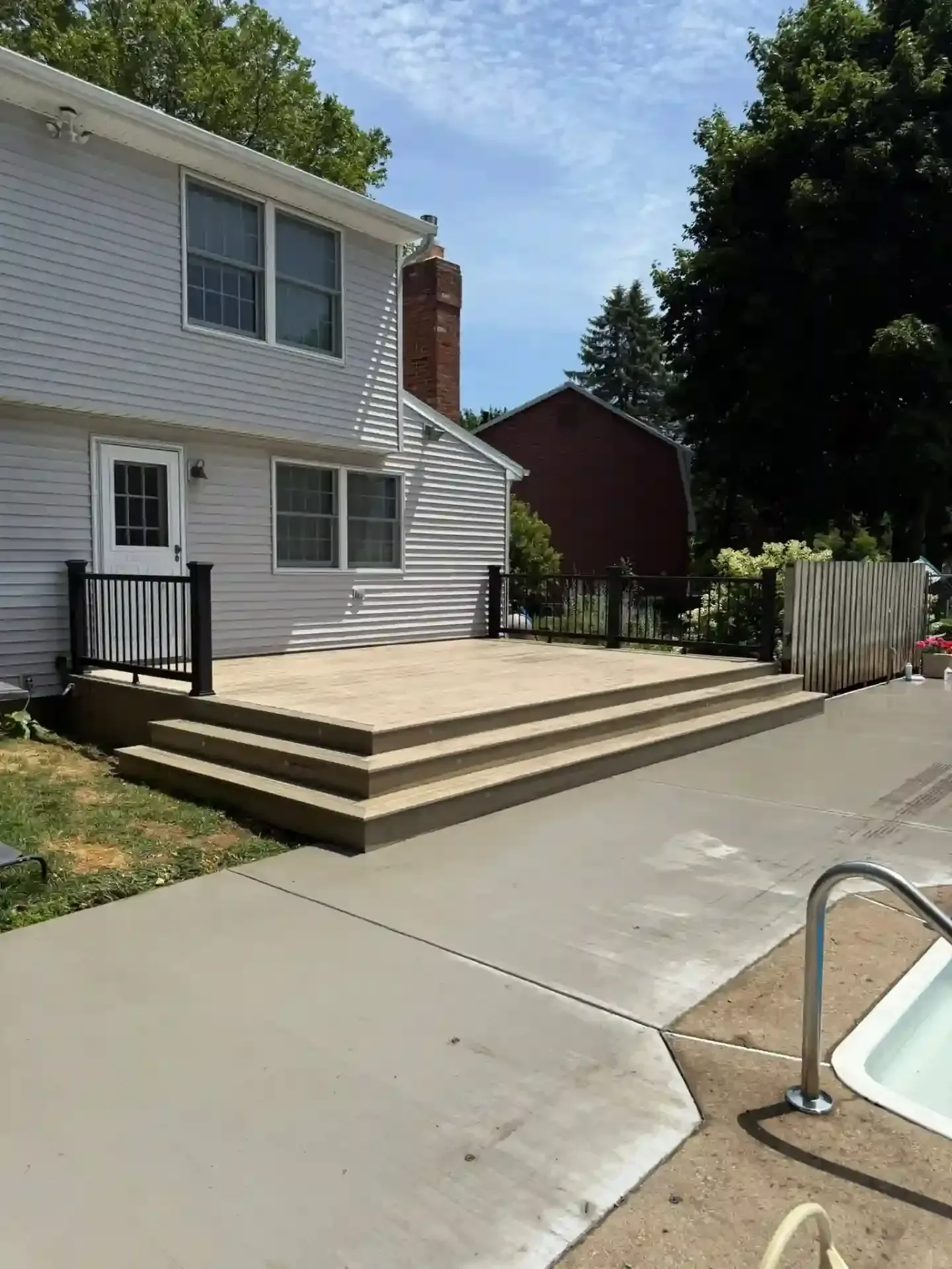 A freshly built wooden porch with siding and railing, in front of a white house.