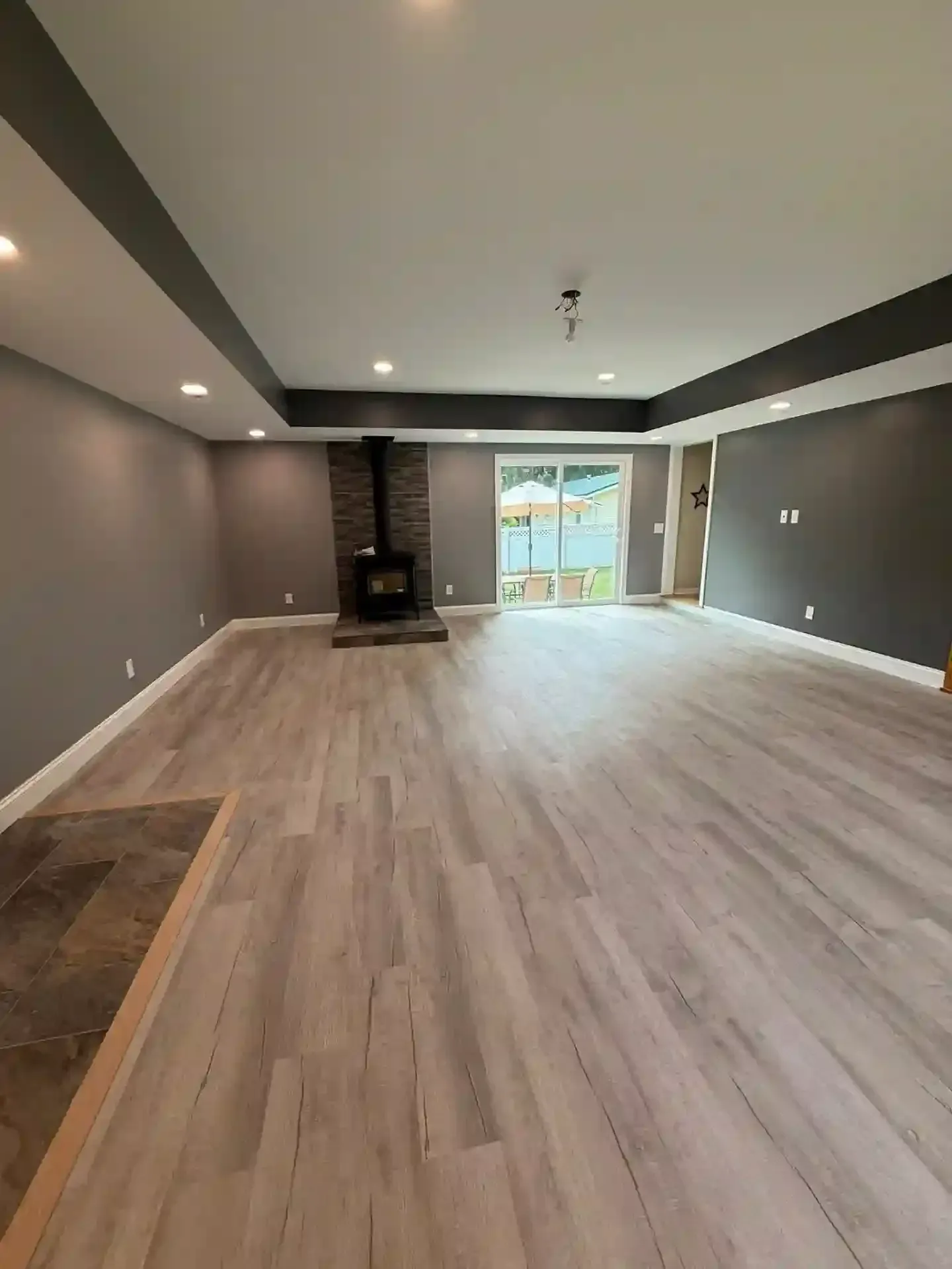 Empty room with wood-look flooring, gray walls and ceiling, a fireplace, and sliding glass door.
