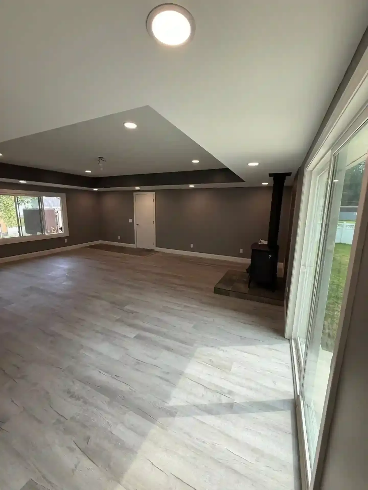Spacious living area with gray walls, light wood flooring, and recessed lighting; sliding glass door.