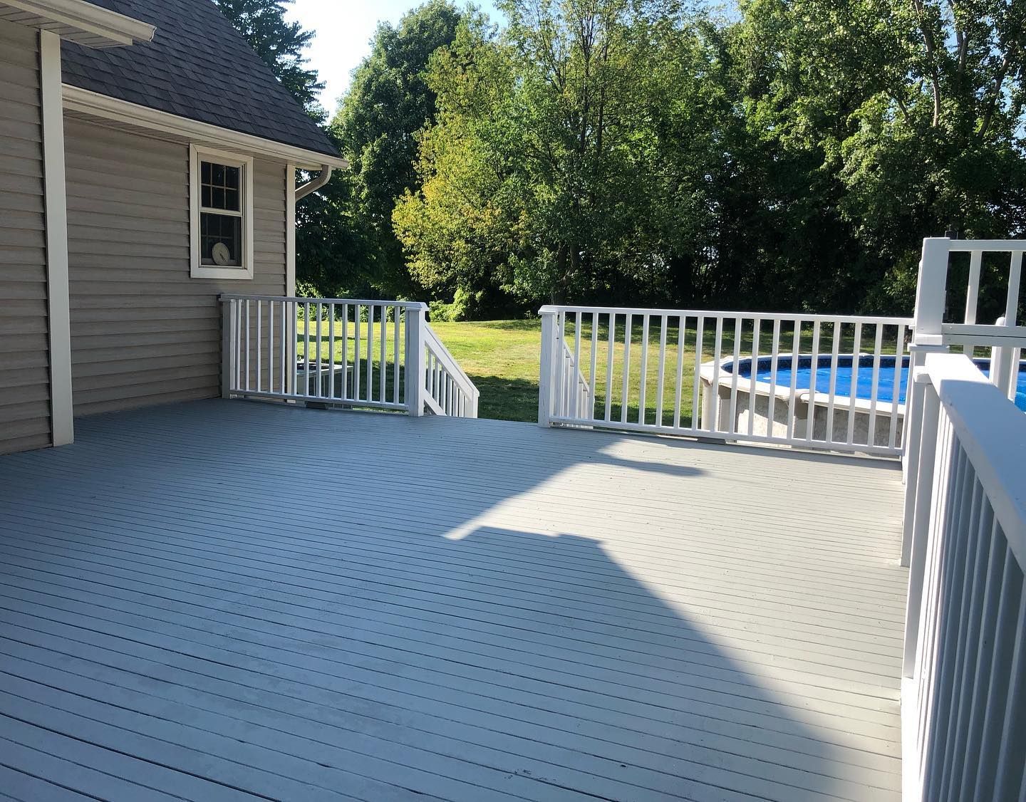 Deck with gray, circular pattern, white railing, and above-ground pool in a backyard.