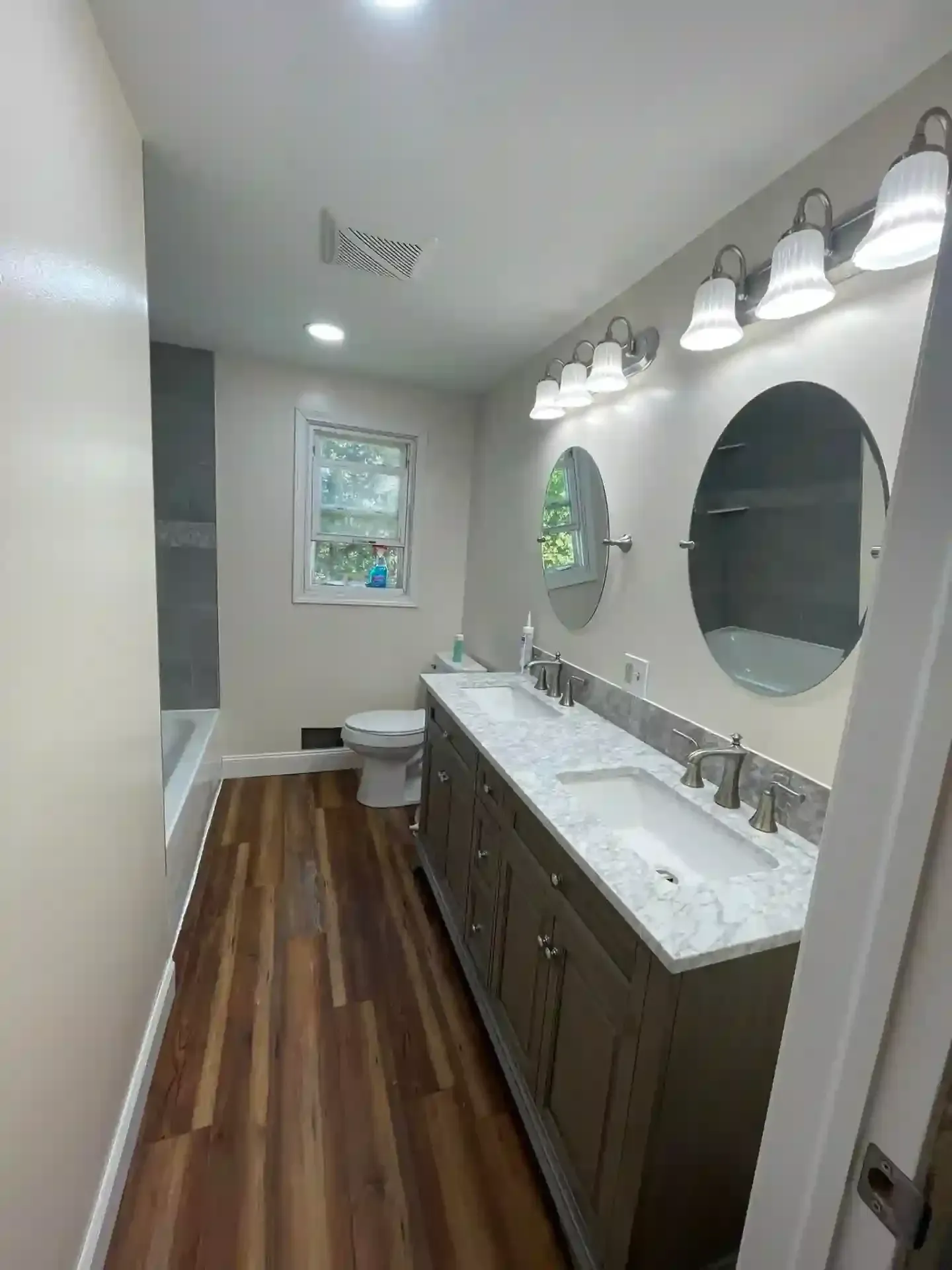 Bathroom with wood-look floor, double vanity, round mirrors, and a window.