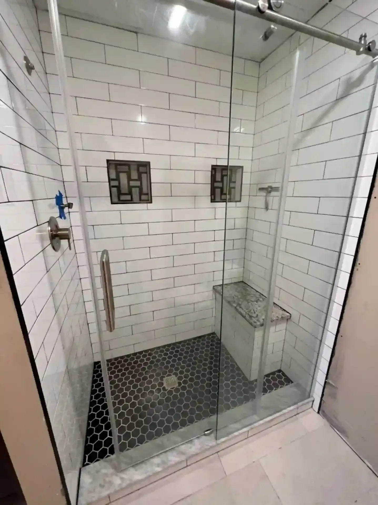 A glass-enclosed shower with white subway tile walls, a dark hexagonal floor, and a built-in bench.