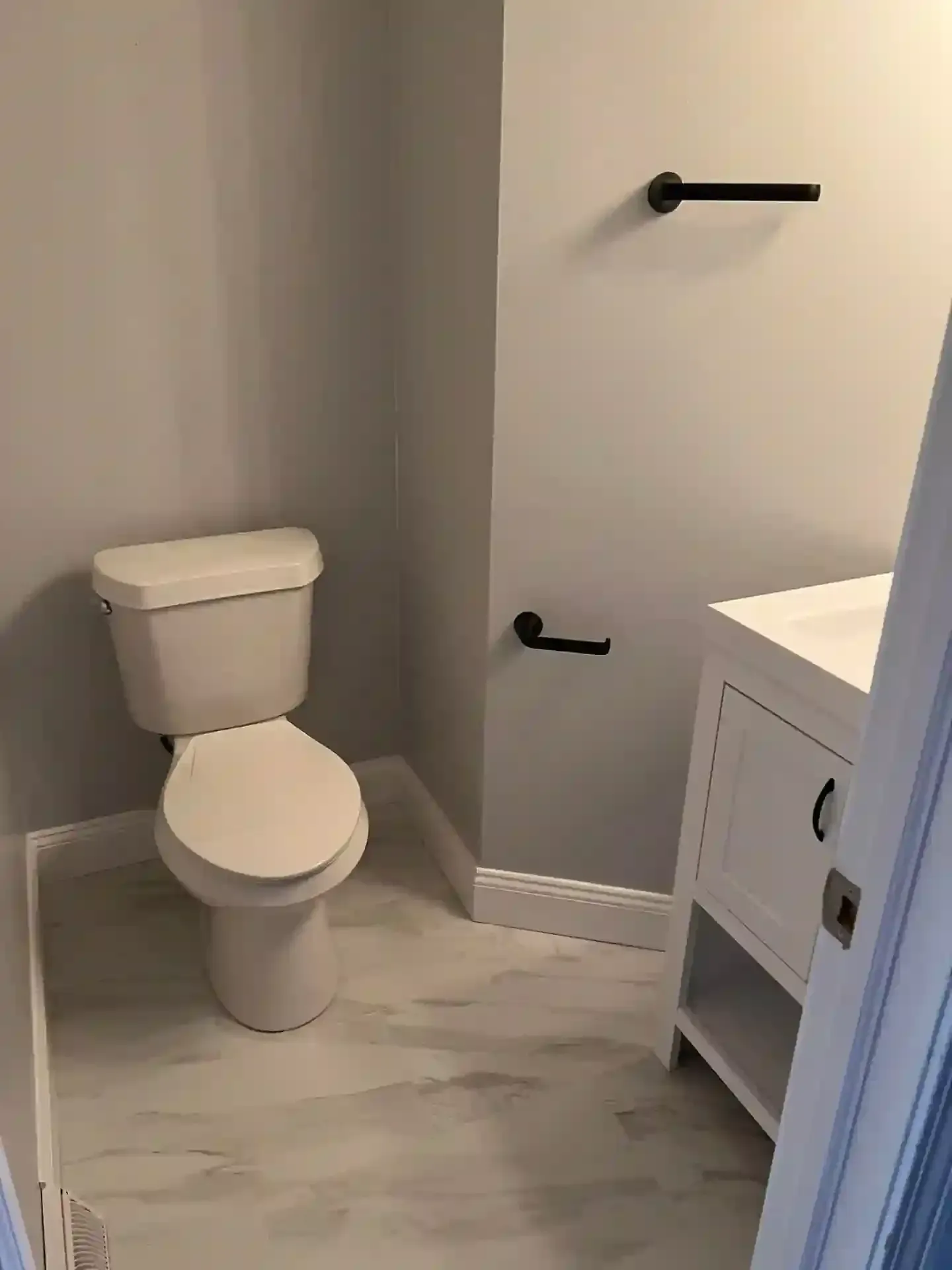Small bathroom with toilet, sink, and towel rack; white and gray color scheme.