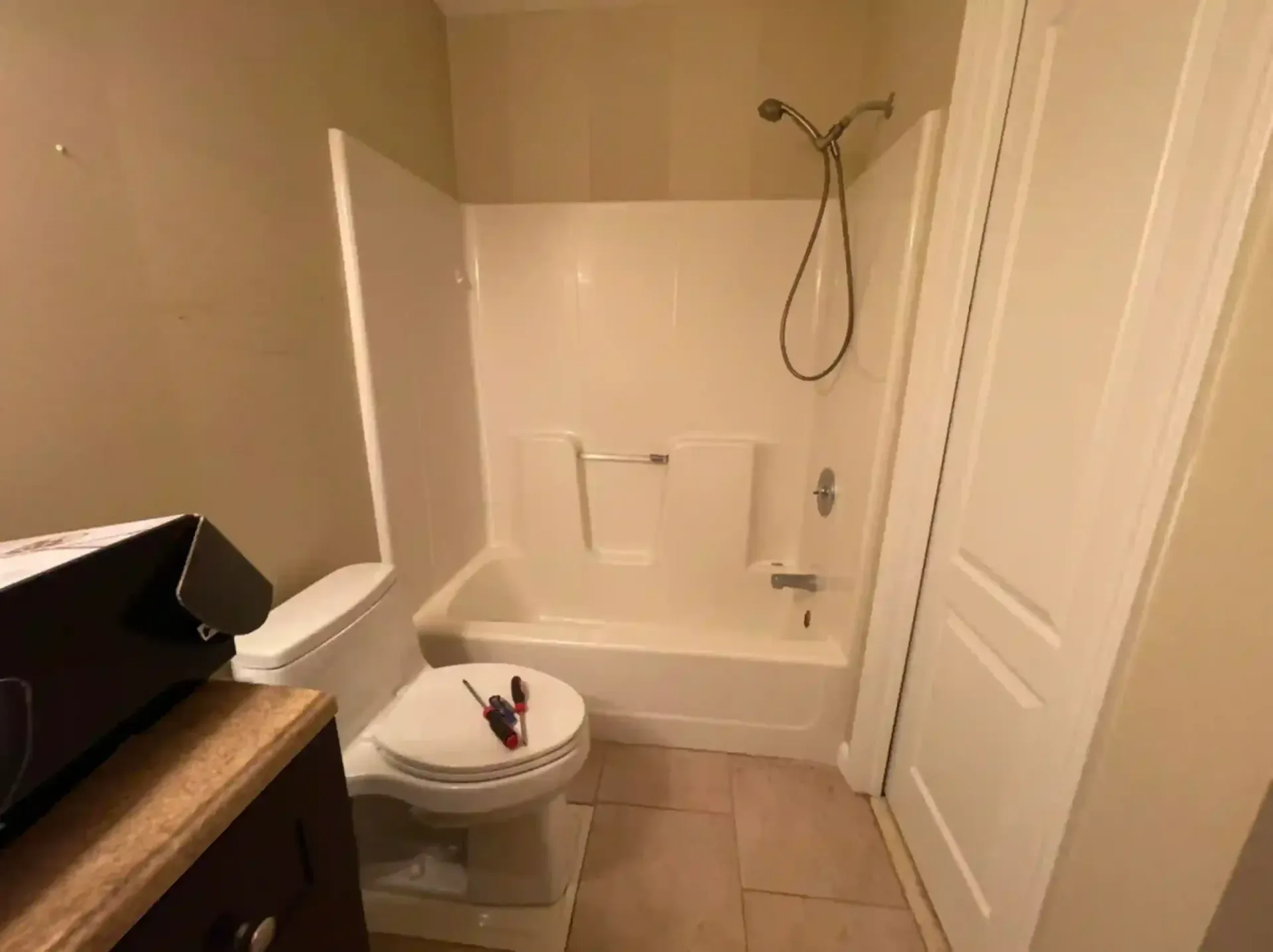 Bathroom with a toilet, shower/tub combo, brown vanity, and a closed white door. Beige walls and floor.