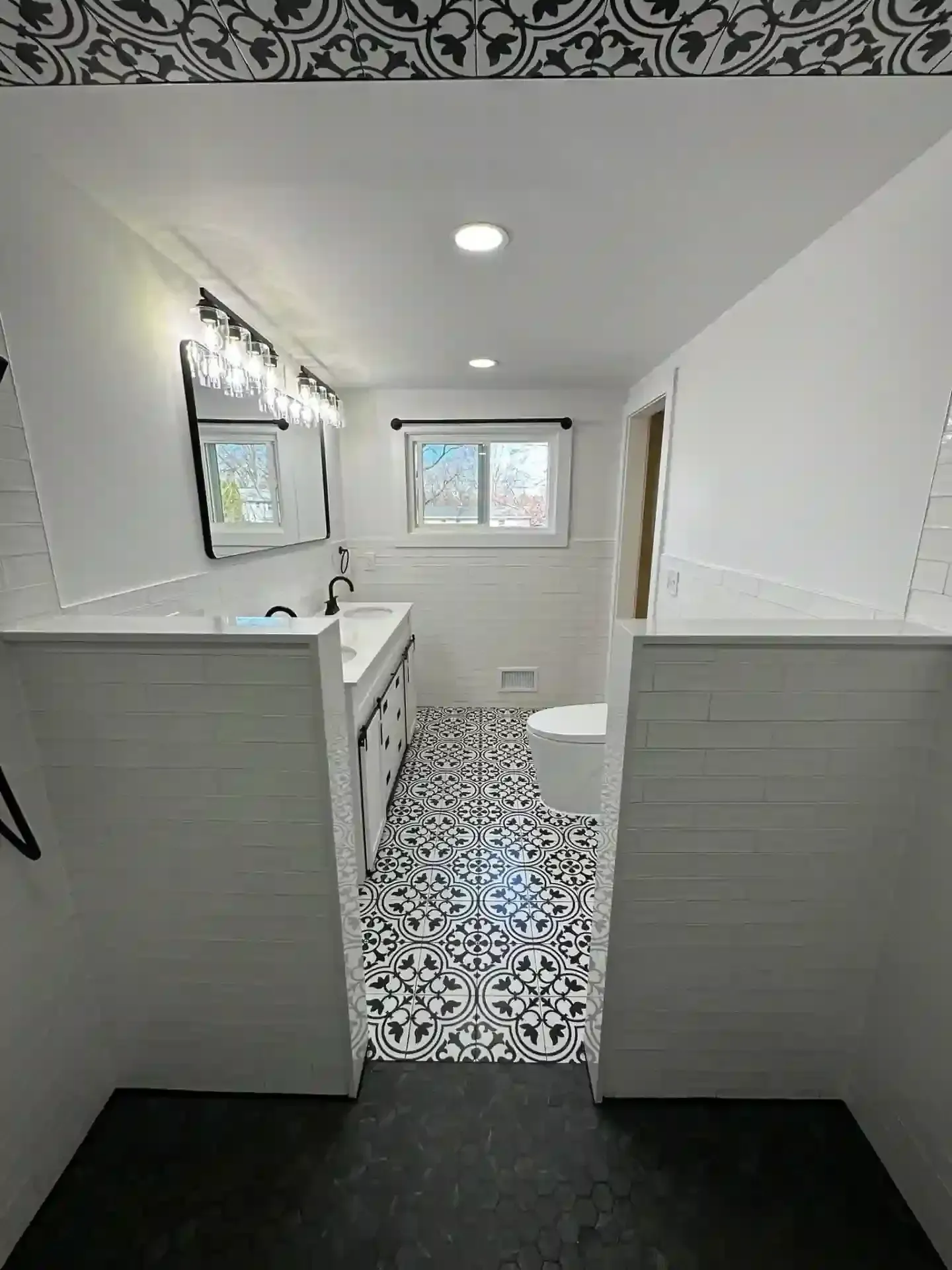 Modern bathroom with patterned black and white floor tiles, white walls, and a black vanity.