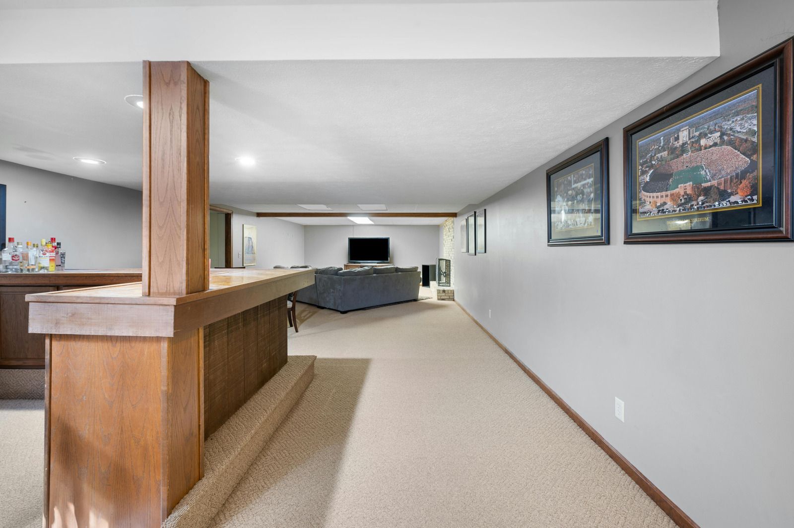Basement with a bar, carpeted floor, and framed pictures on the wall.