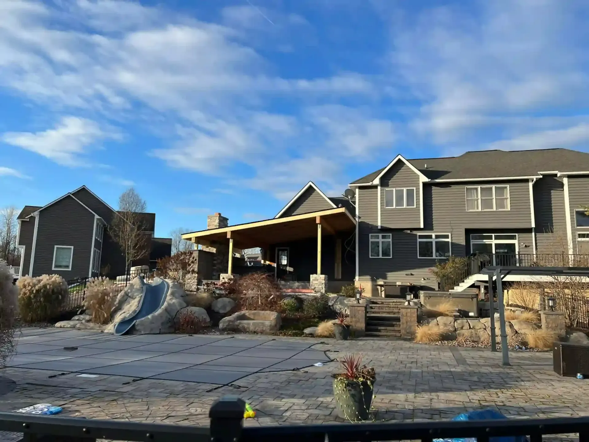 Backyard with gray houses, covered patio, rock landscaping, and a blue sky.