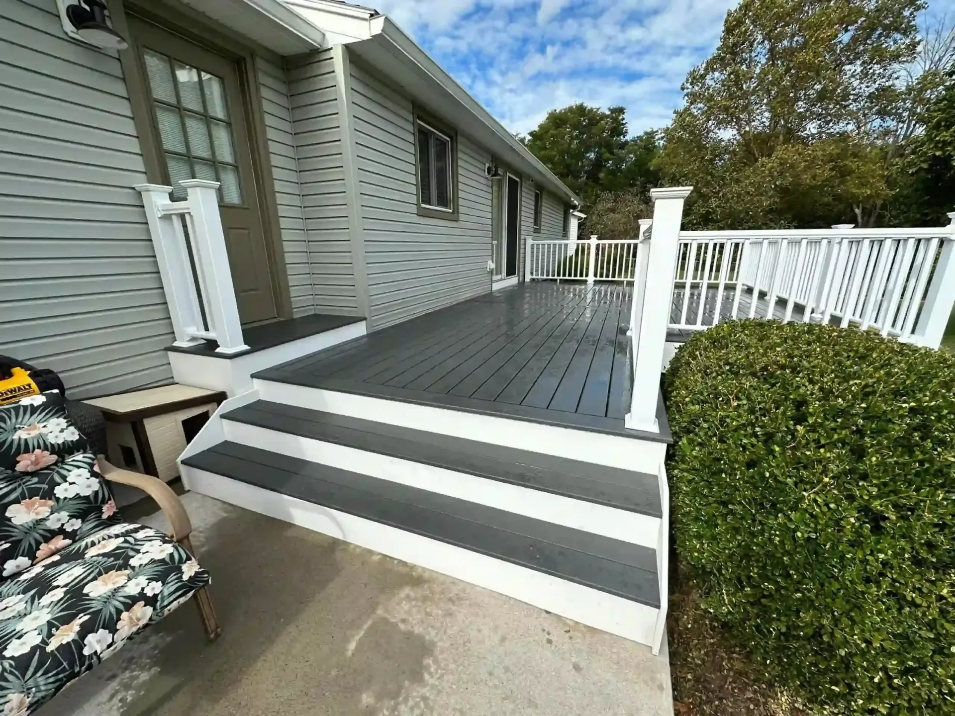 Gray and white deck with steps leading to a house, next to green bushes.
