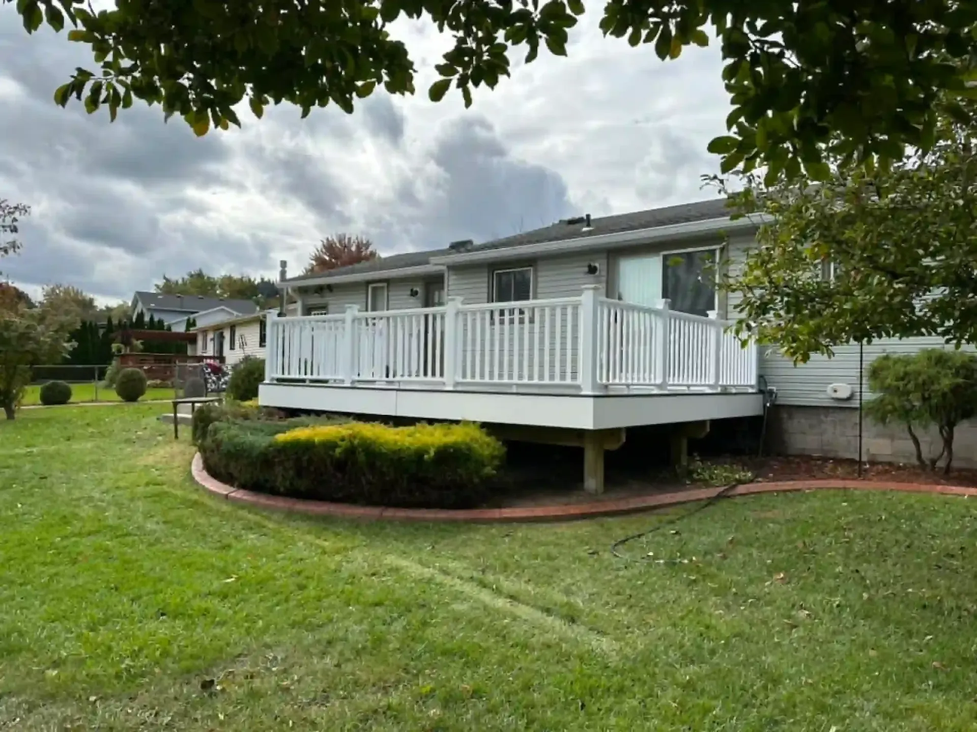 White deck with railing on a building, green lawn, cloudy sky.
