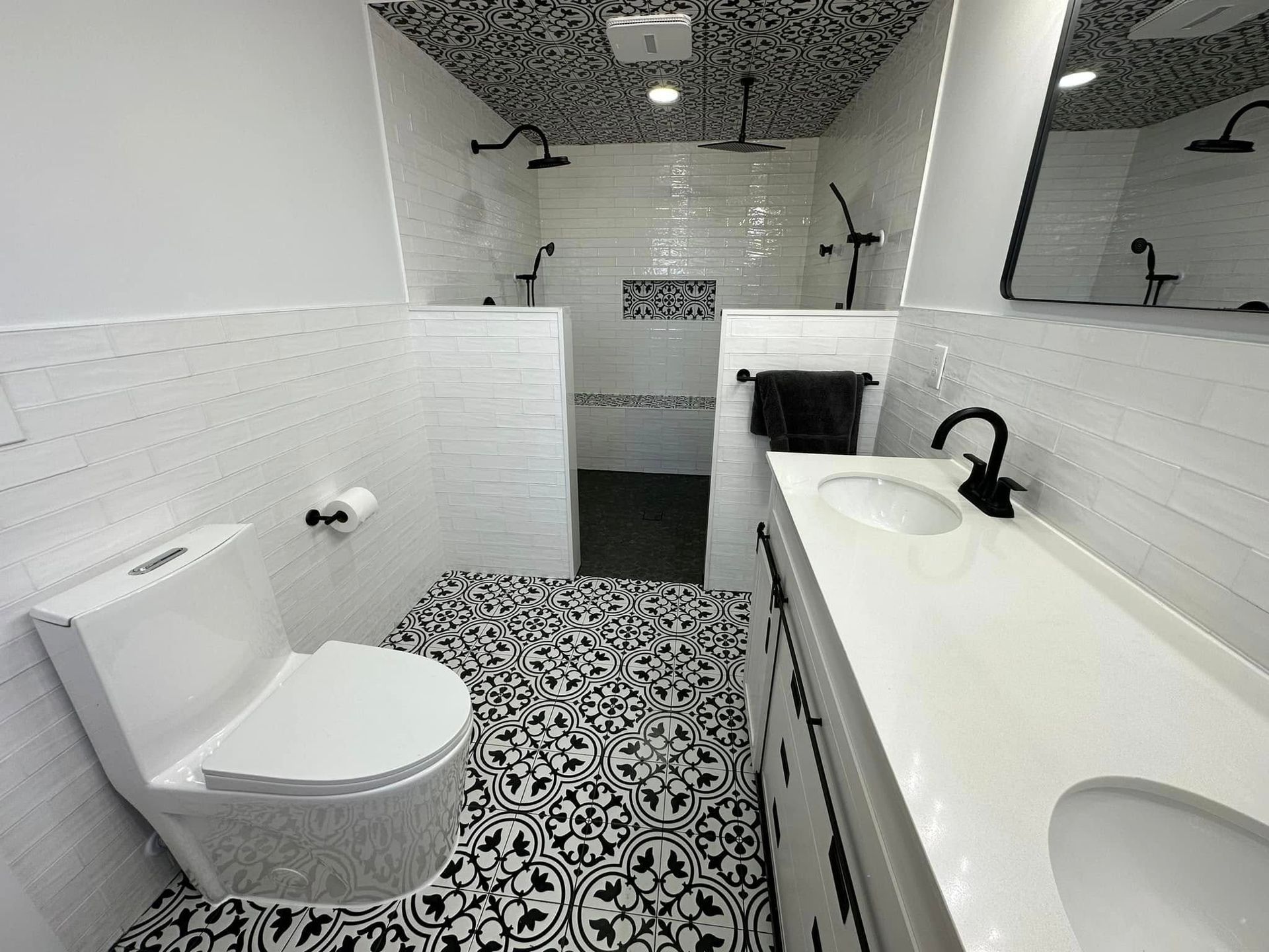 Modern bathroom with black and white tile floors and walls, two showers, and a double sink.