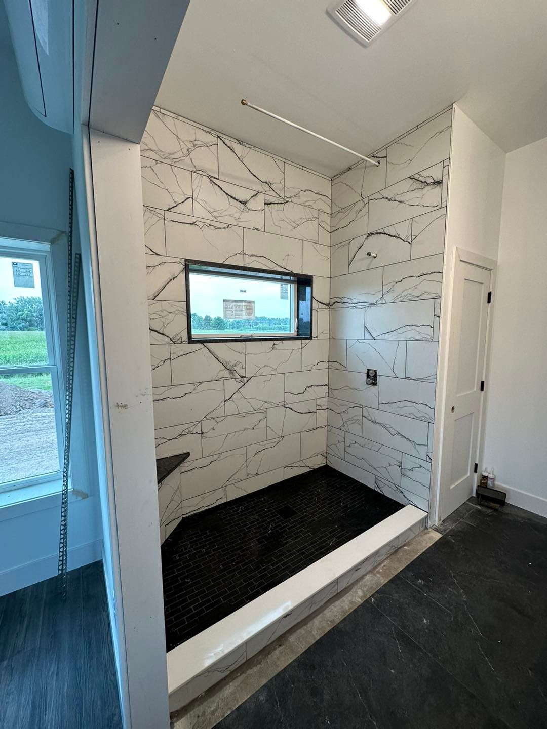 Modern shower stall with white and black tile, window, and black shower floor.