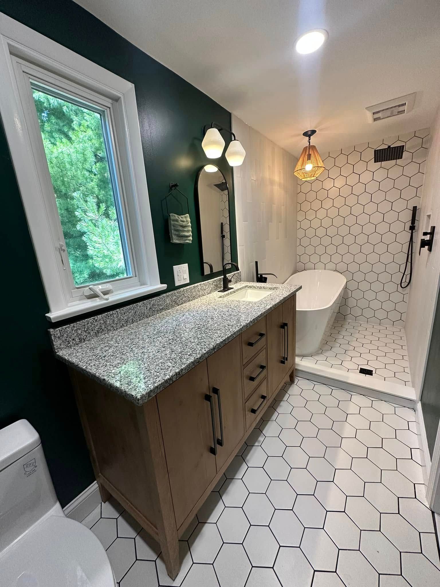 Modern bathroom with dark green and white walls, hexagon floor tiles, and a freestanding tub.