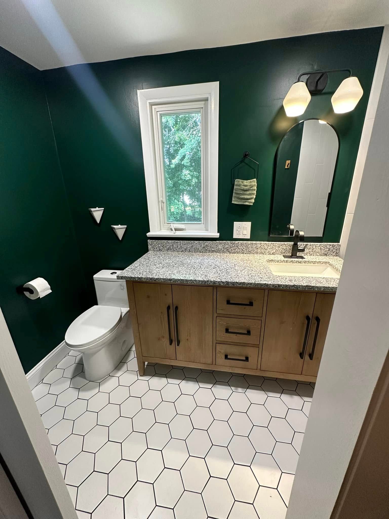 Bathroom with dark green walls, wood vanity, white hexagon tile floor, and a window.
