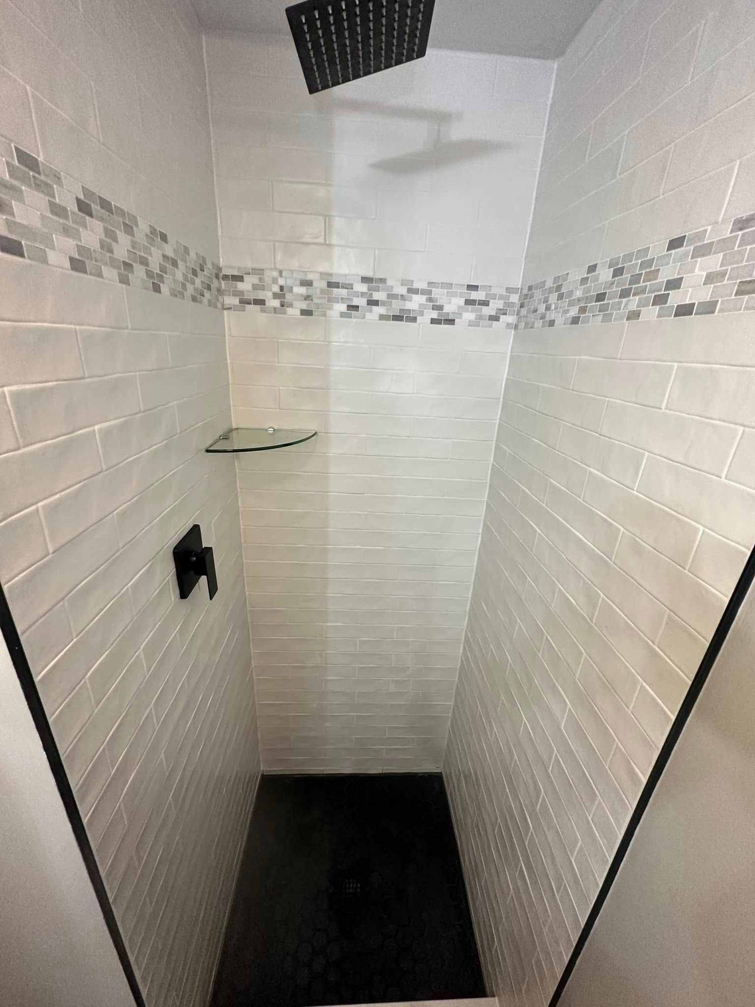 Modern shower with light gray tiled walls, black shower head and fixtures, and a black floor.