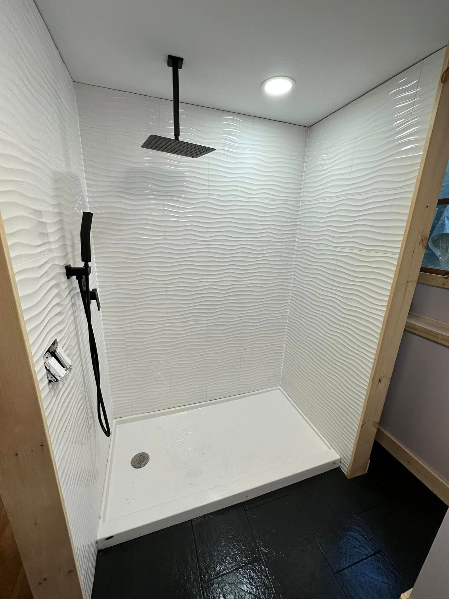 White tile shower with black fixtures and dark floor.