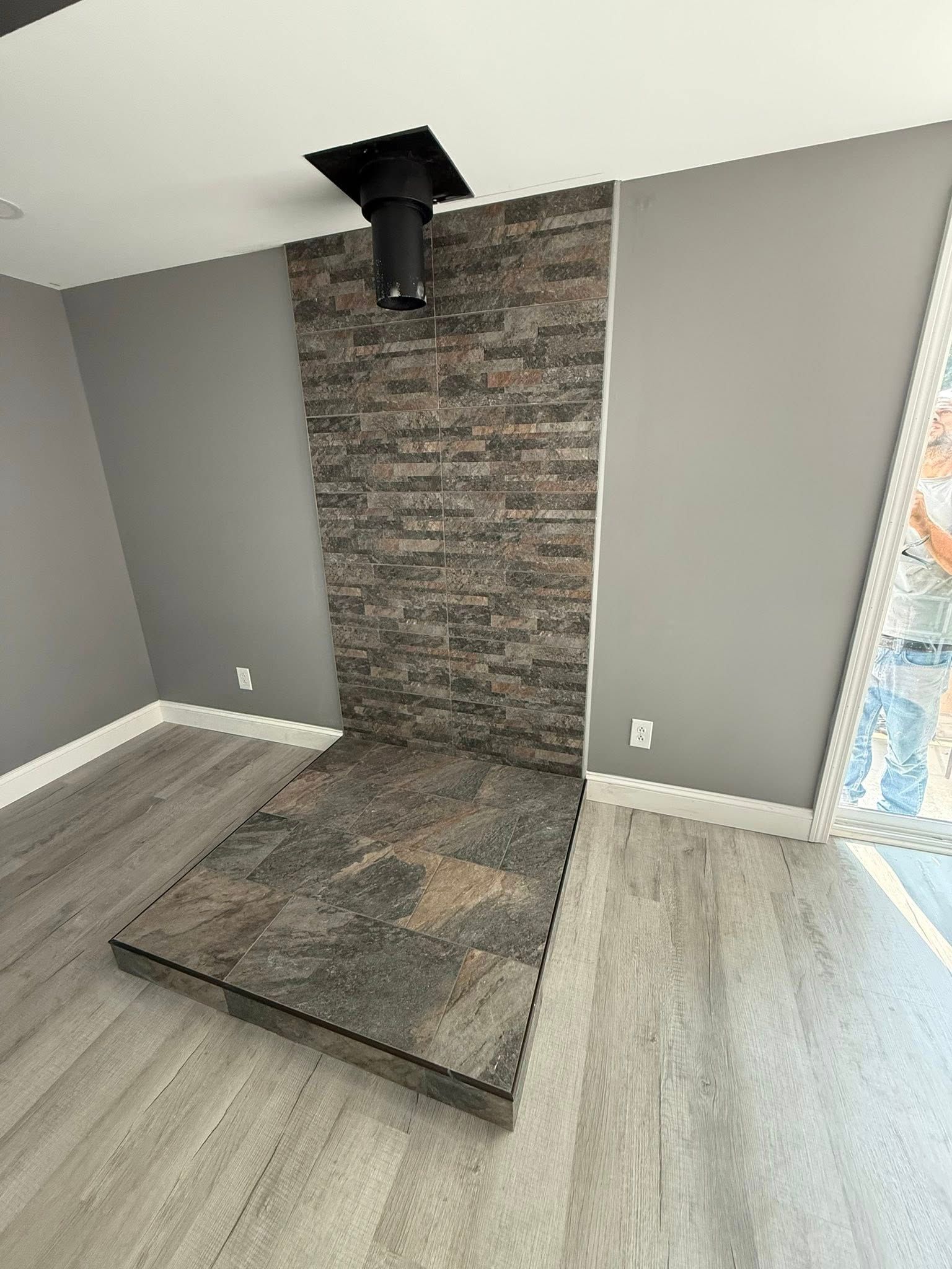 Modern fireplace with stone facade and dark chimney against gray wall and light wood-look floor.