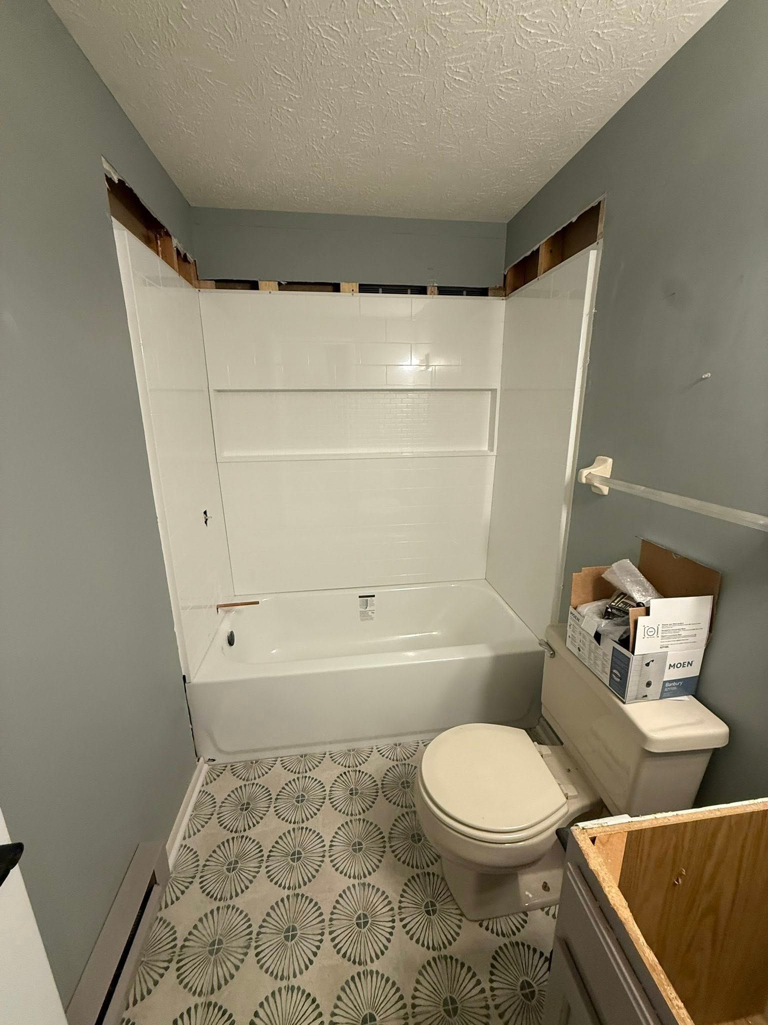 Bathroom remodel, white shower surround, blue walls, patterned floor, toilet, sink cabinet, and exposed ceiling.