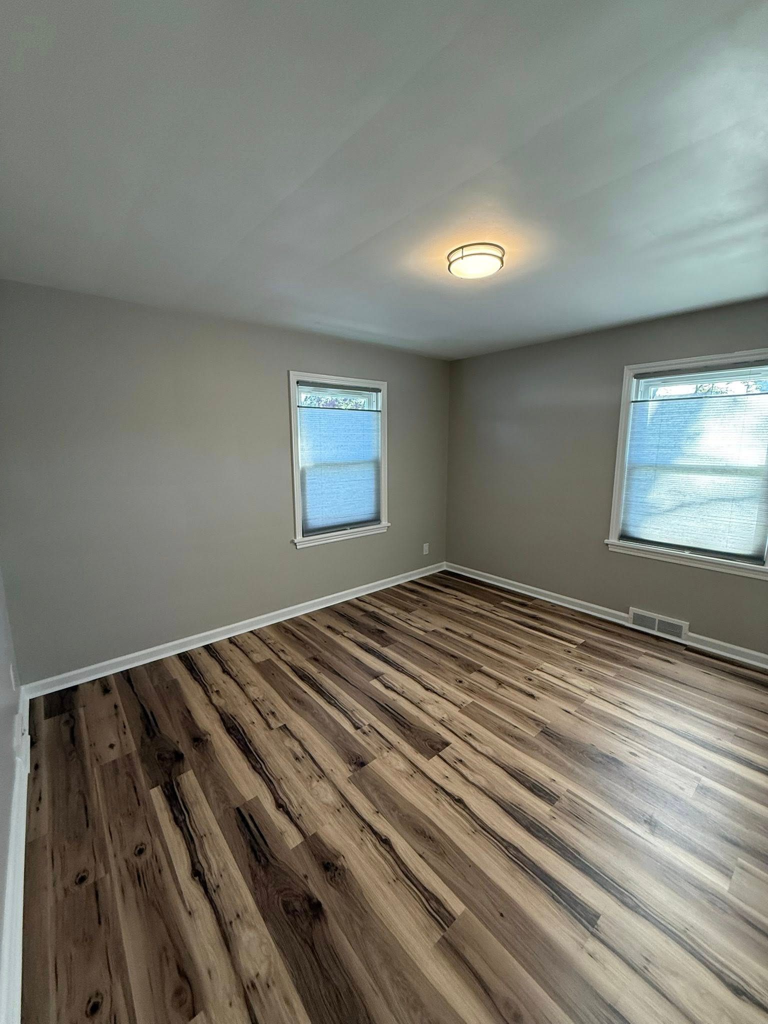 Empty room with wood-look floor, gray walls, two windows, and a ceiling light.