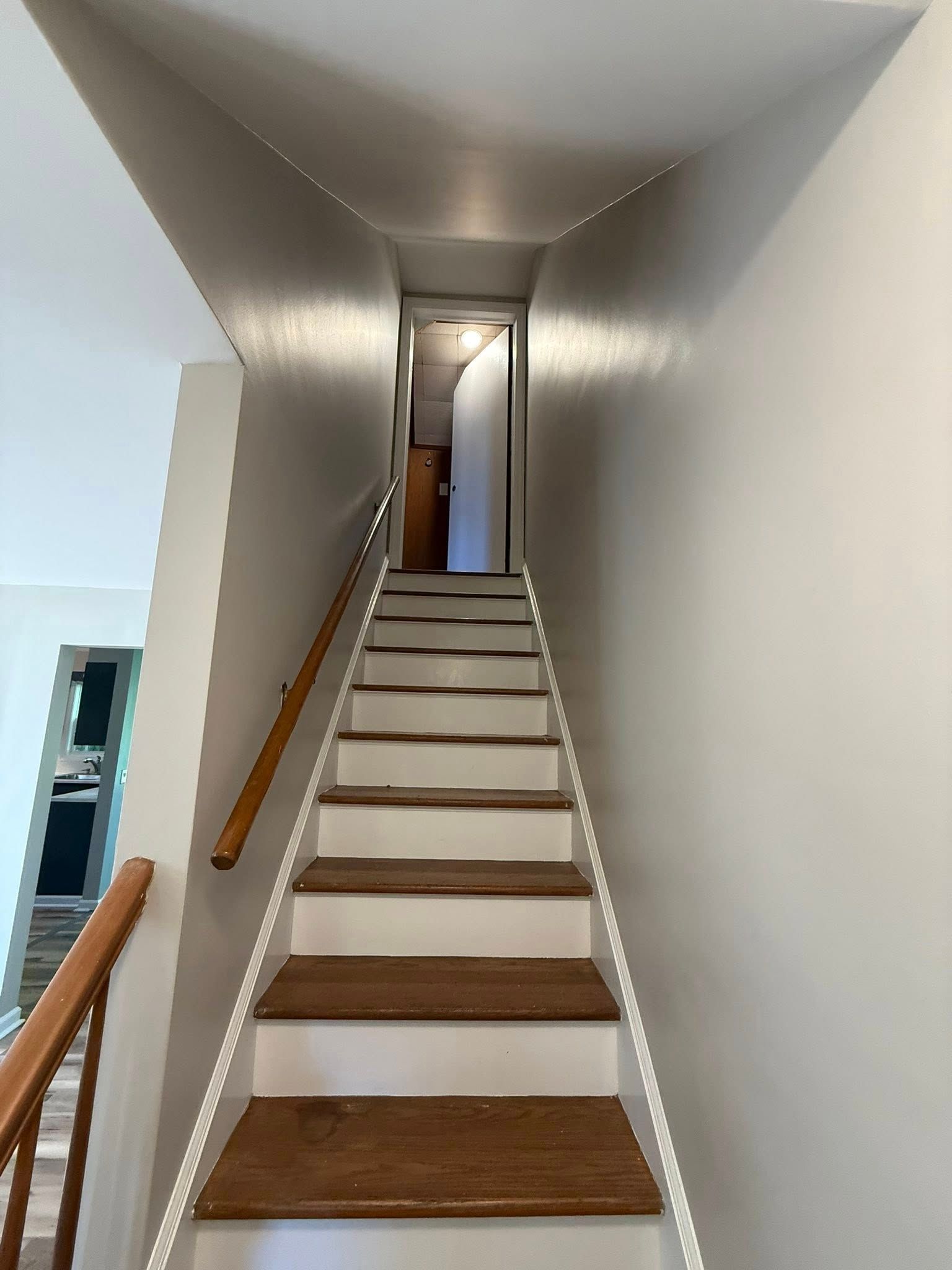 Staircase with wooden steps and a handrail, leading up to a doorway. White walls and neutral colors.