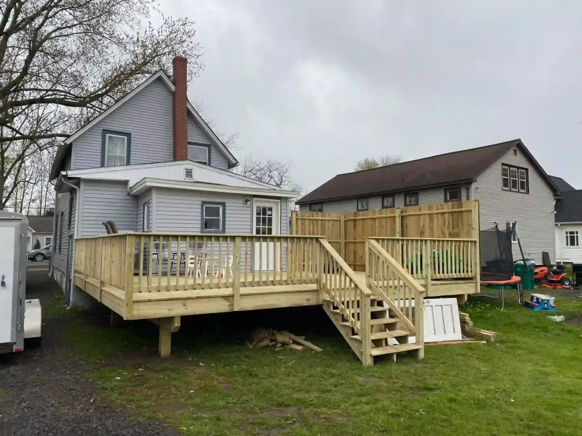 Newly built wooden deck attached to a light blue house. Stairs lead down to a grassy yard on an overcast day.