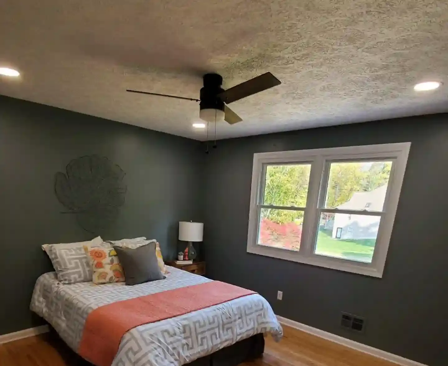 Bedroom with dark green walls, a bed with orange accents, and a ceiling fan.