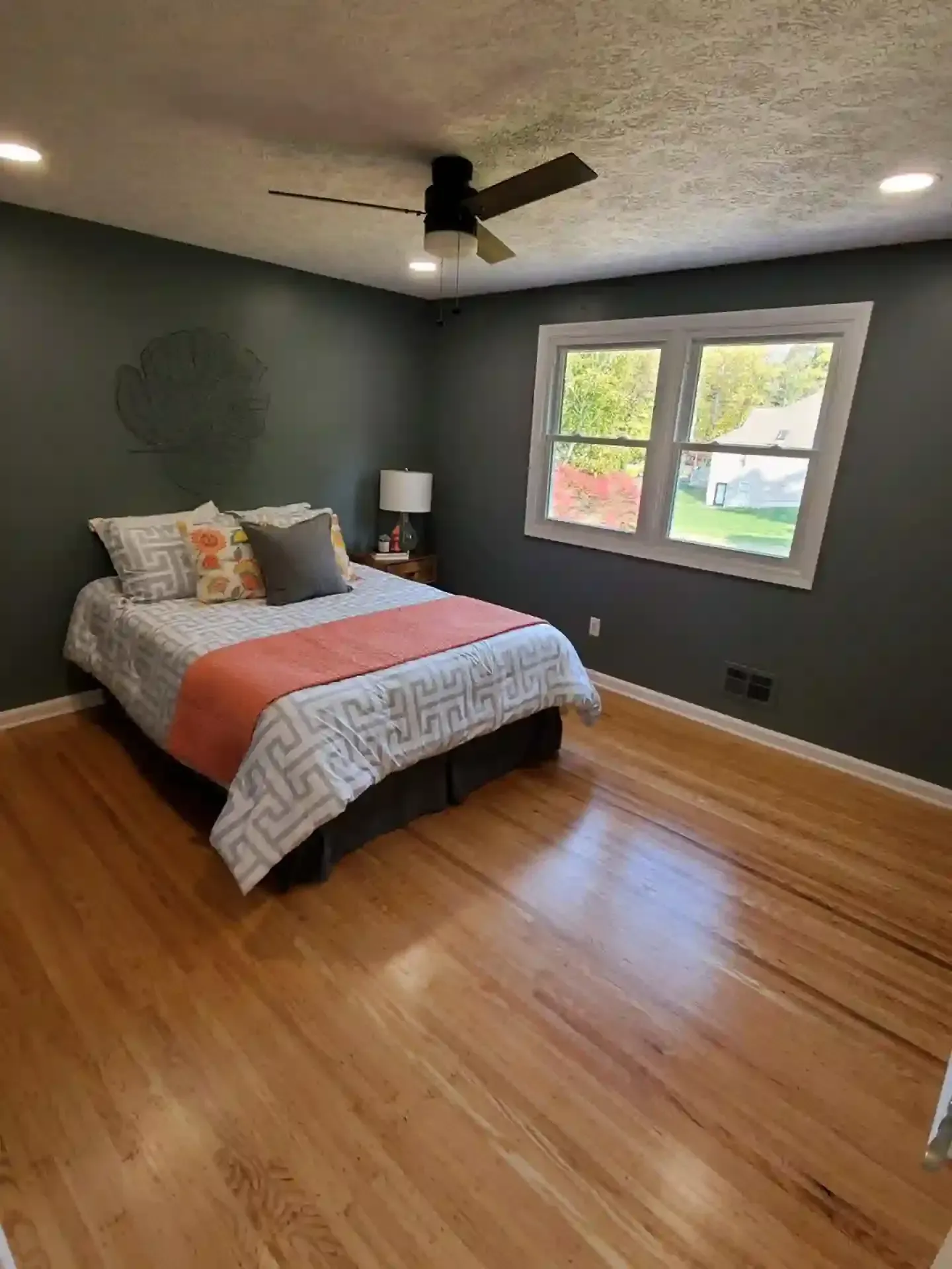 Bedroom with dark green walls, hardwood floor, bed with orange and patterned bedding, and a window.