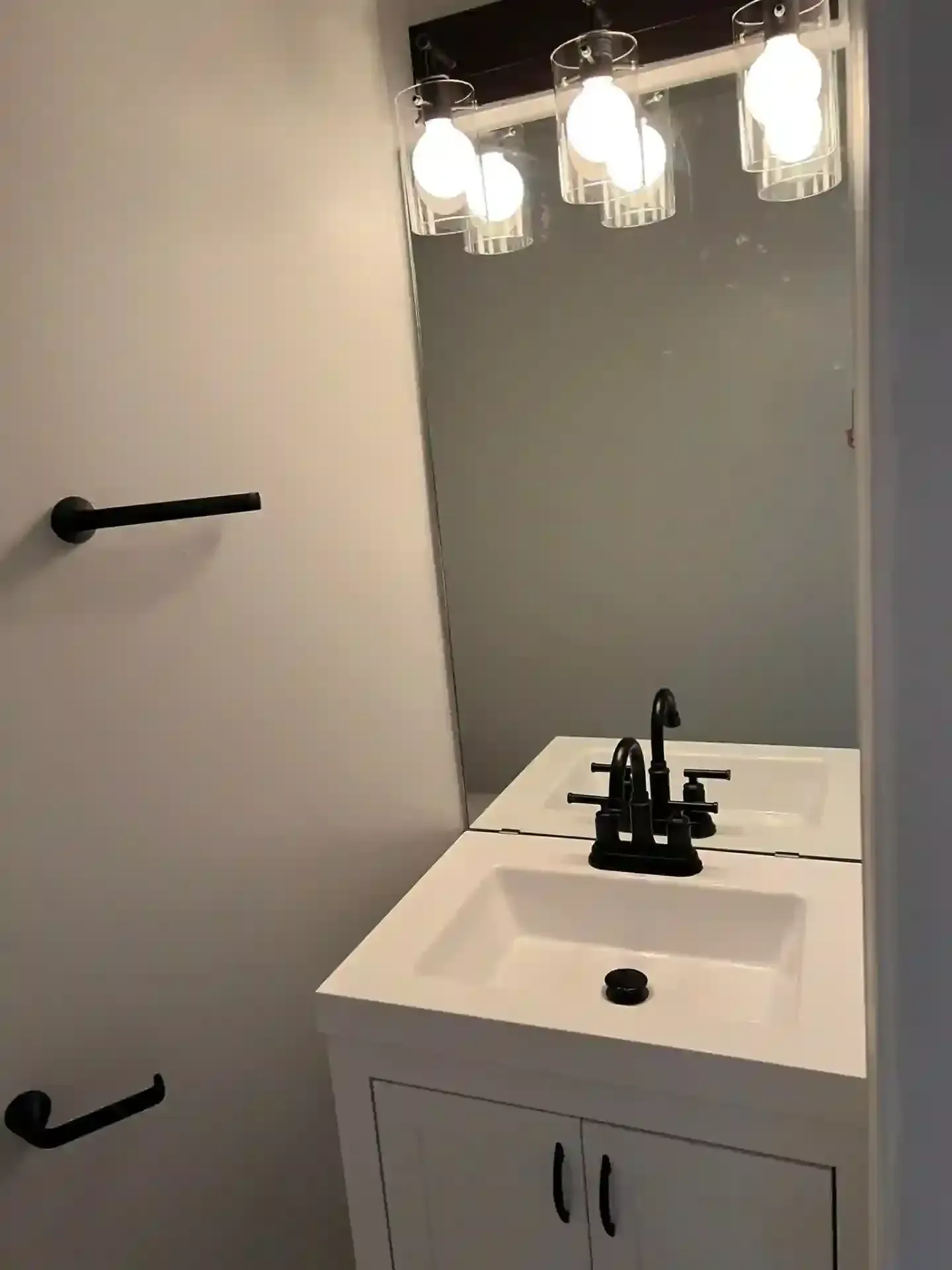 Small bathroom with white vanity, black fixtures, and mirror with light fixture.