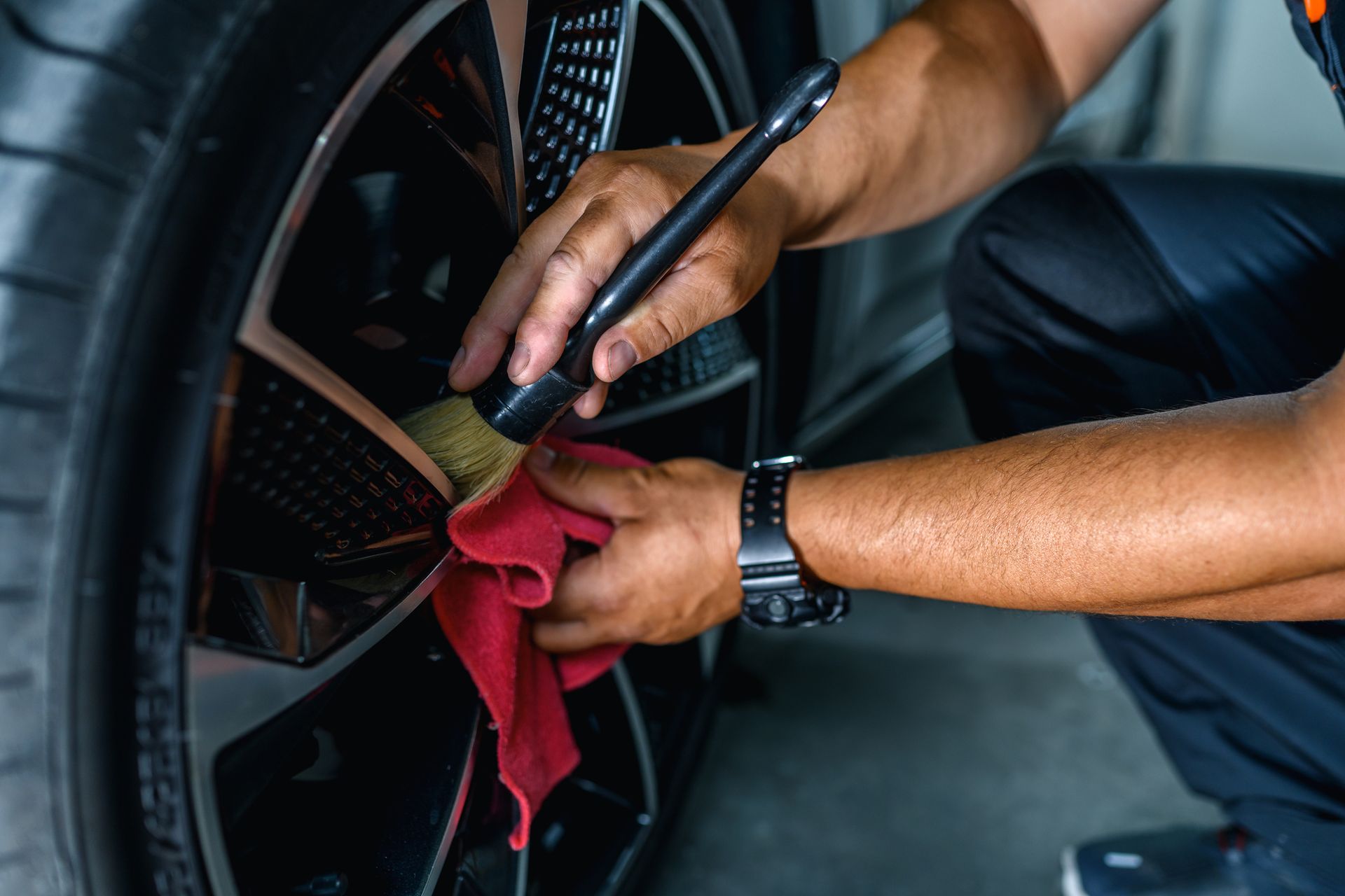 A Man Is Cleaning a Car Wheel with A Brush and A Towel - Parma, OH - Family First Car Care