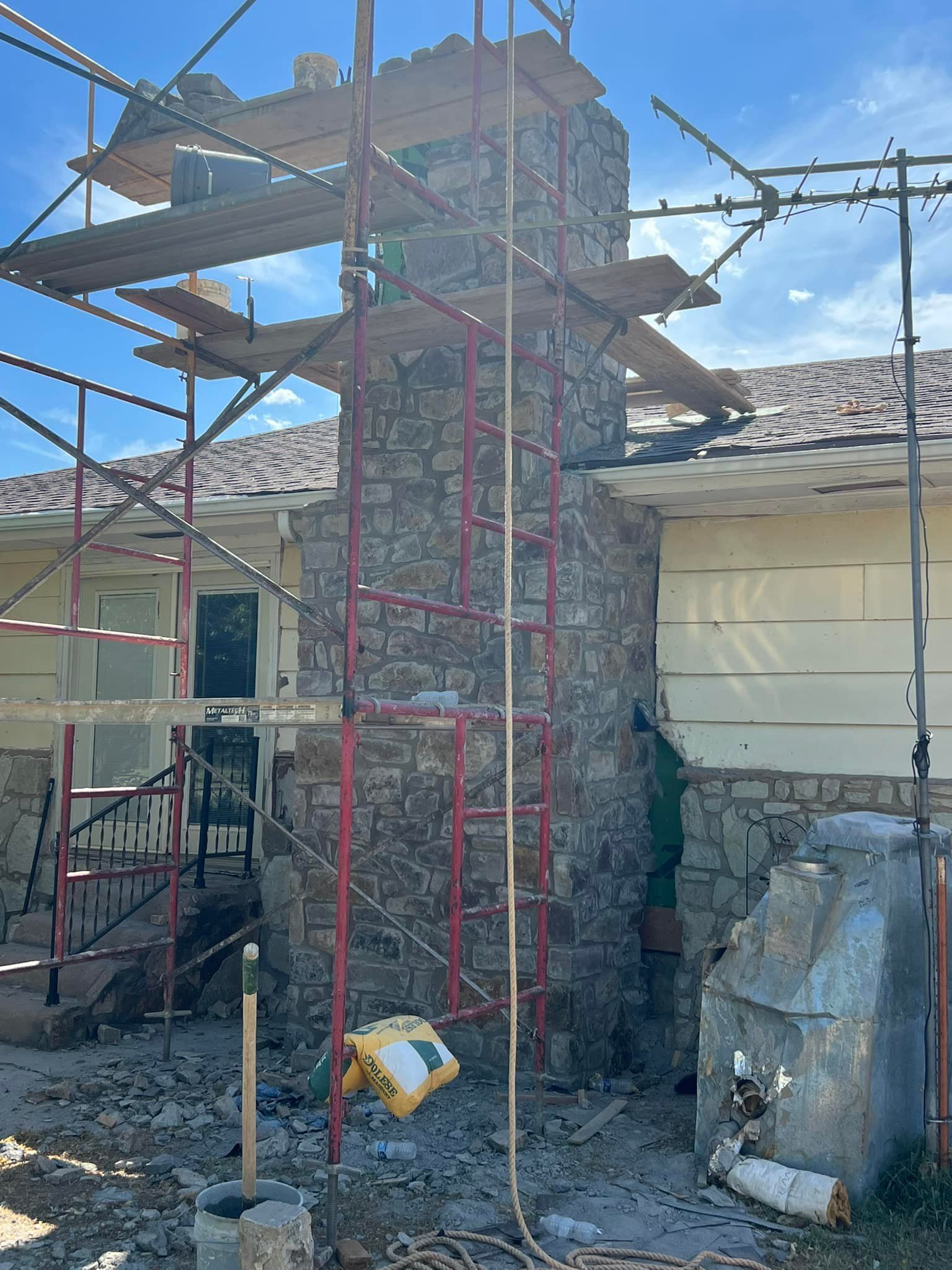 Chimney under construction, surrounded by scaffolding. The chimney is made of stone and is attached to a house. Chimney under construction, surrounded by scaffolding. The chimney is made of stone and is attached to a house.
