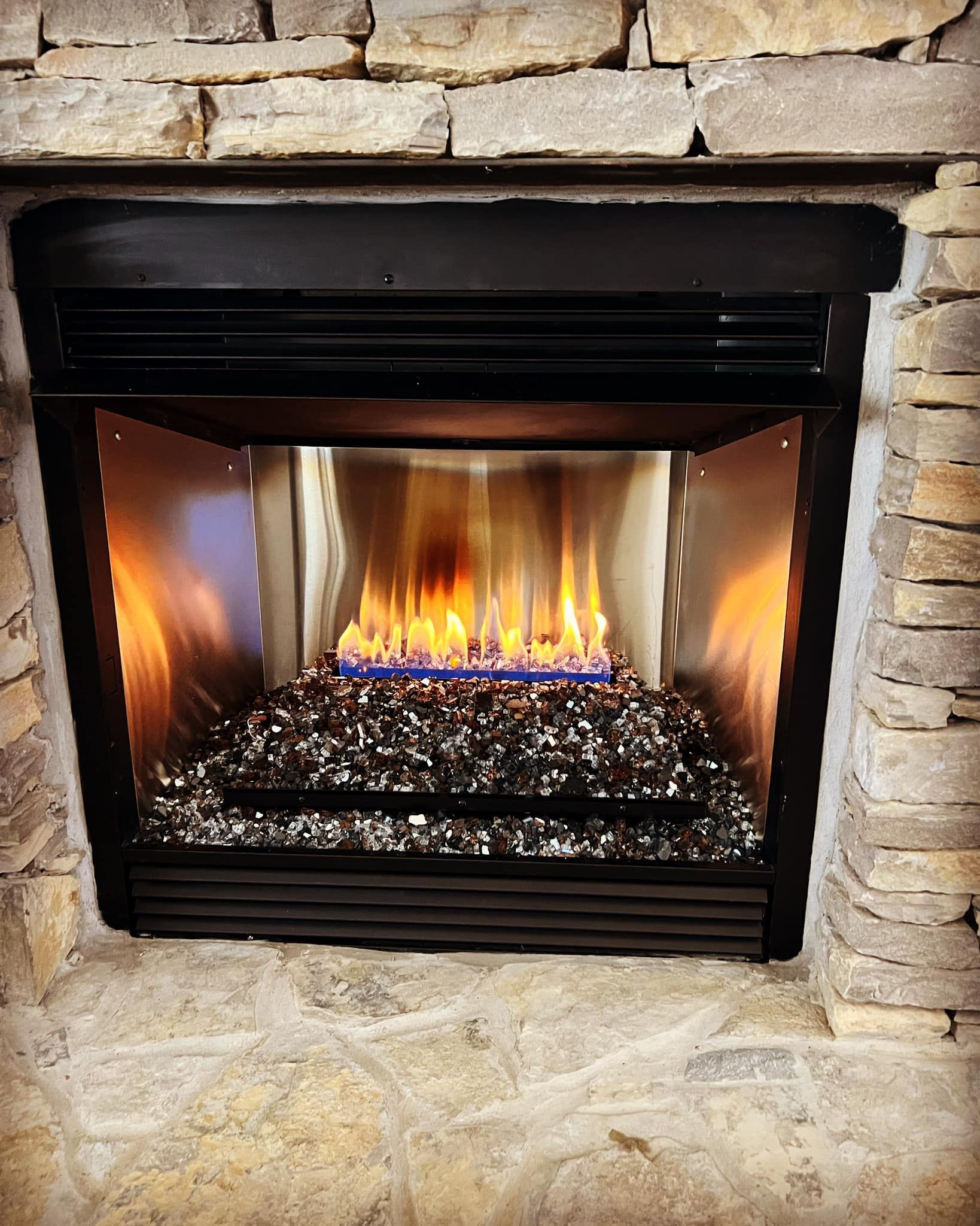 Fireplace with flames and black glass stones, set in a stone surround, black metal trim. Fireplace with flames and black glass stones, set in a stone surround, black metal trim.