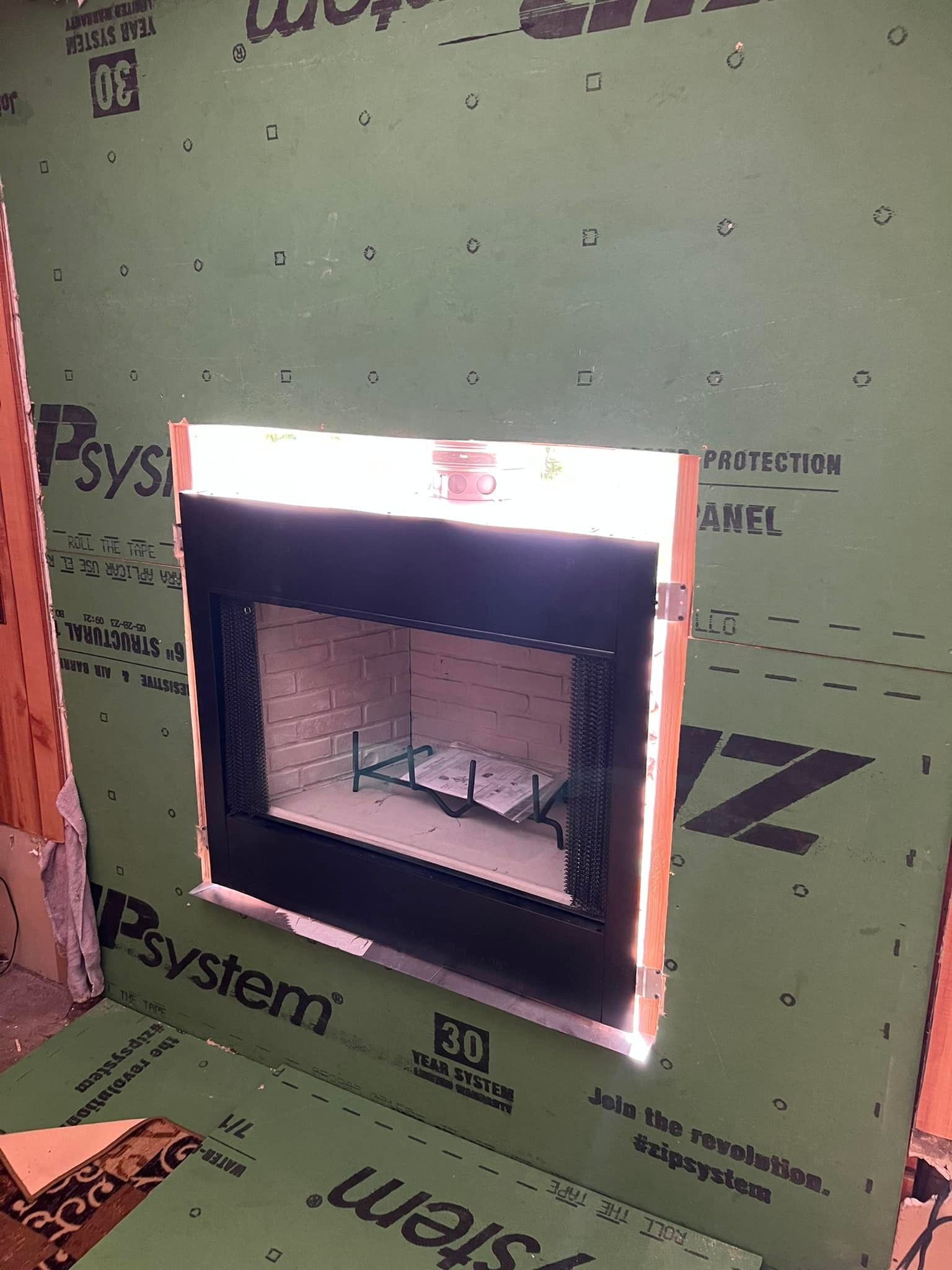 A black fireplace insert installed in a wall opening, surrounded by green sheathing.
