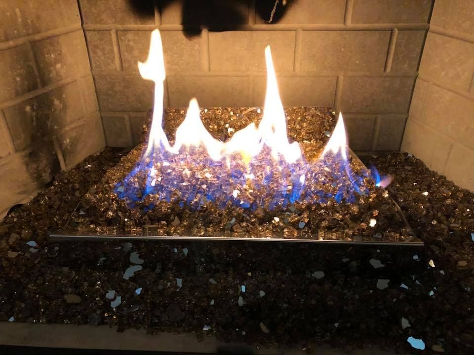 Fireplace with flames rising from blue and gold glass rocks within a brick hearth.