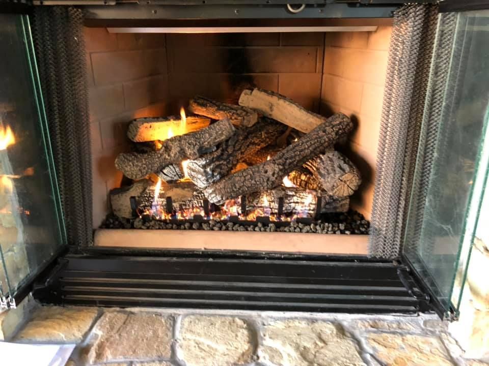 Fireplace with burning gas logs, glass doors, mesh screens, and stone hearth.