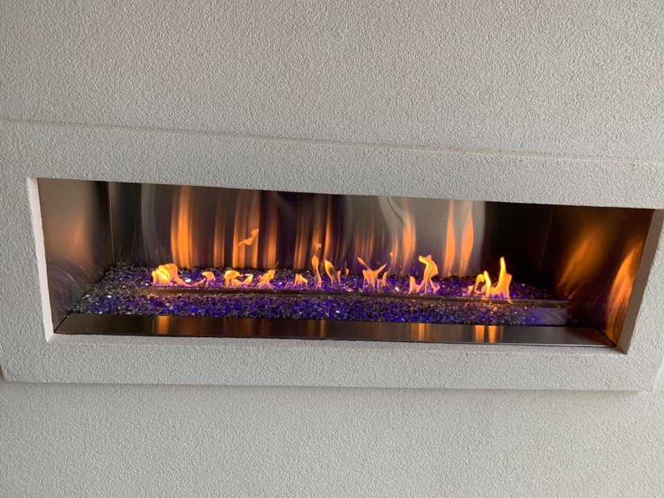 Built-in fireplace with blue glass and orange flames, set in a white speckled wall. Built-in fireplace with blue glass and orange flames, set in a white speckled wall.