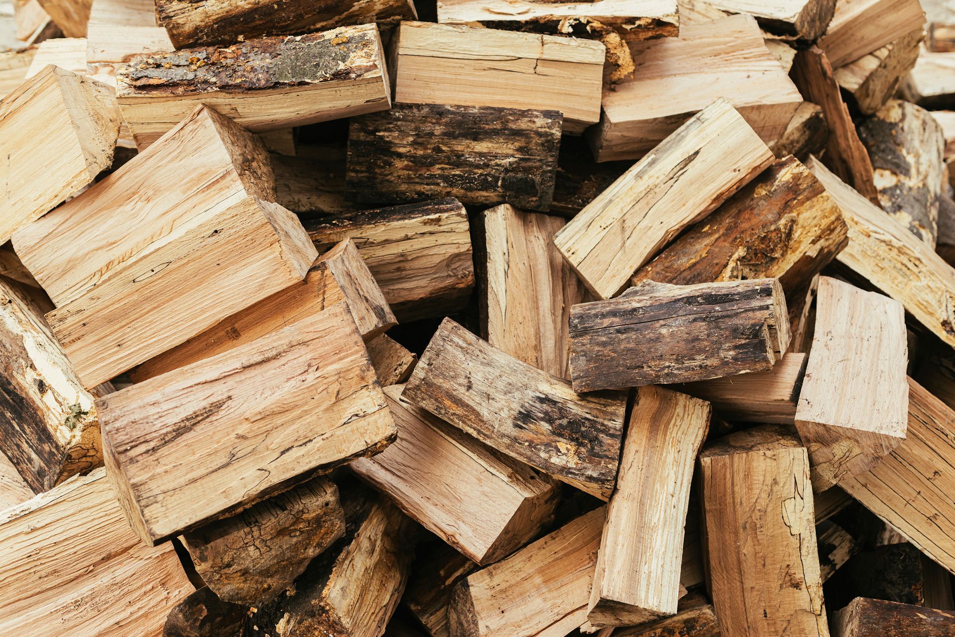 Stack of split firewood logs piled closely together, showing rough bark.