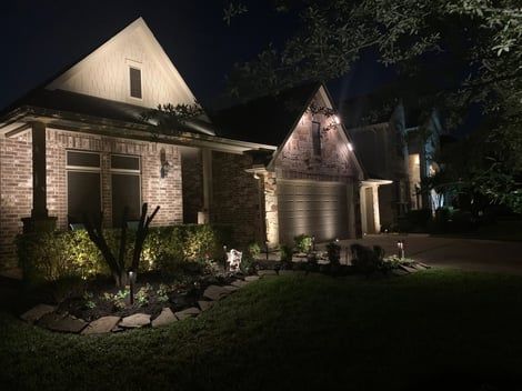Night view of a house with architectural and landscape lighting illuminating the brick and greenery.