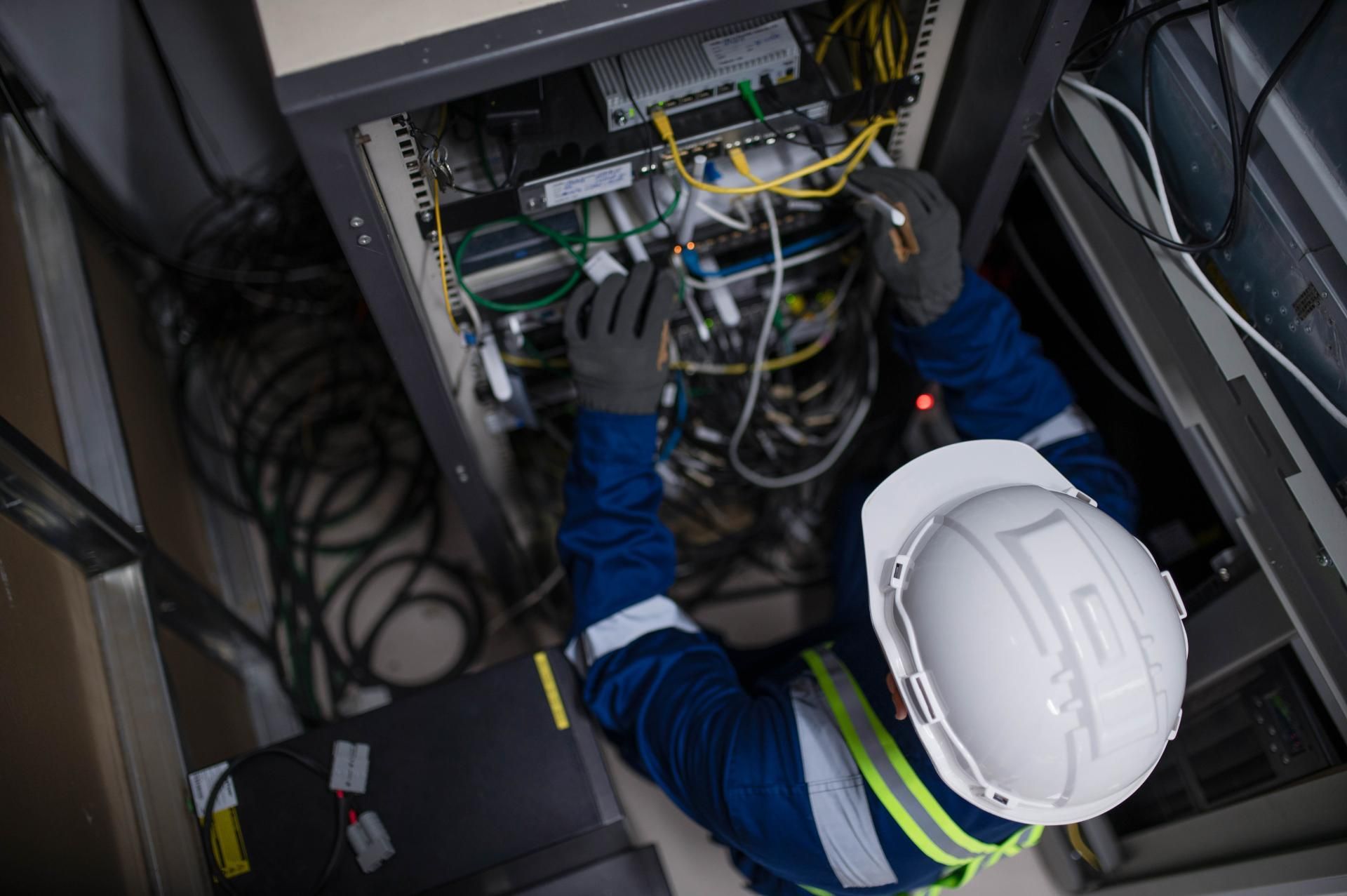 Person in blue jumpsuit and white helmet working on server rack cables.