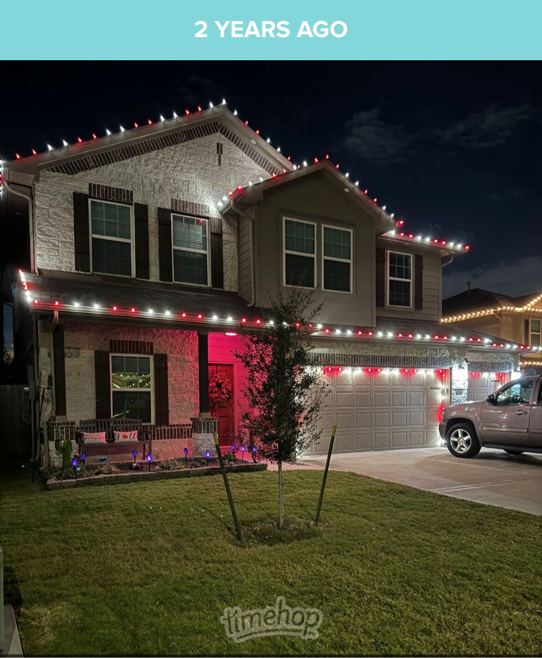House decorated with red and white Christmas lights at night, with a truck parked in the driveway.