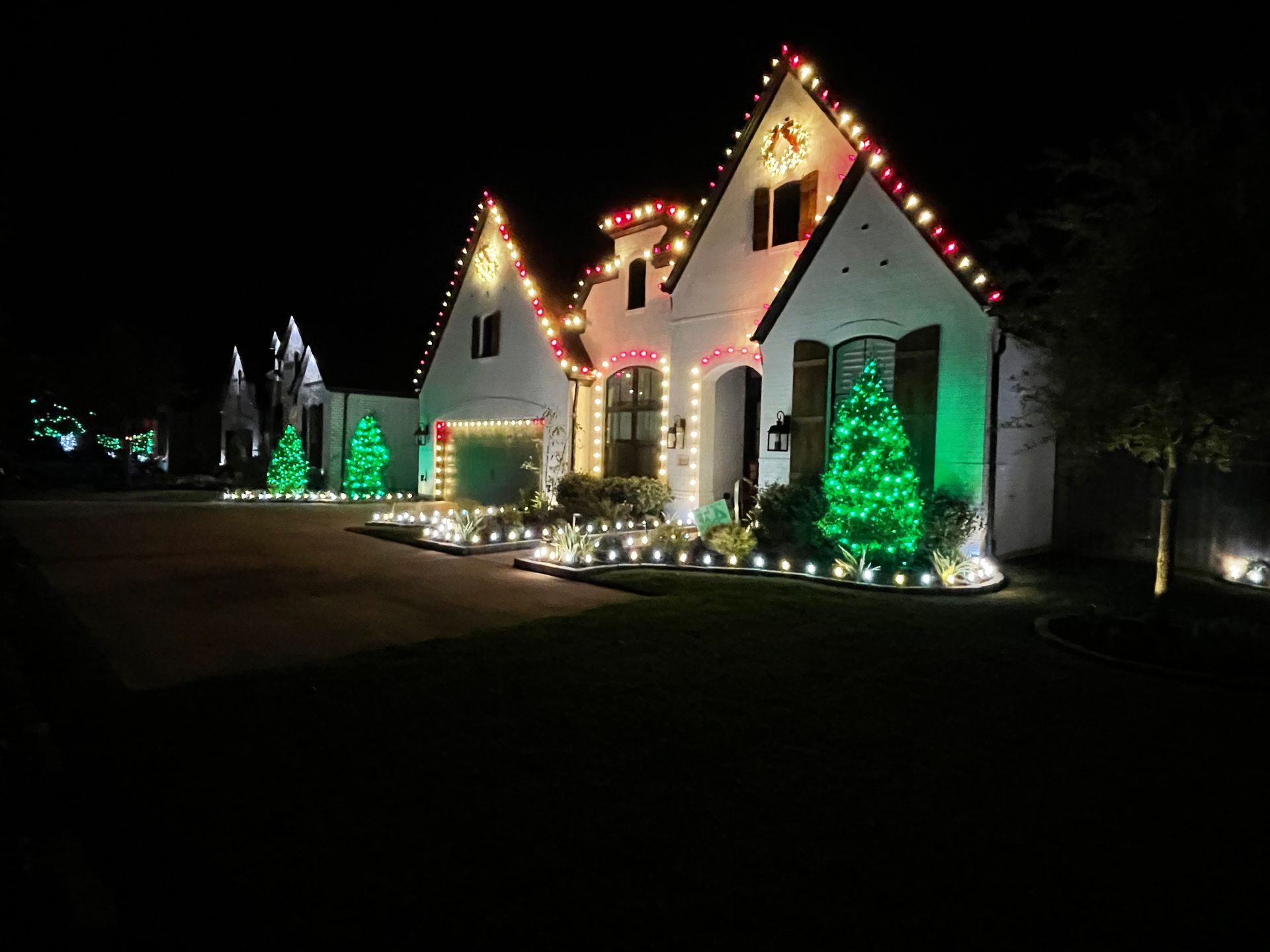 House decorated with Christmas lights at night; red, green, and white lights on the roof, trees, and ground.