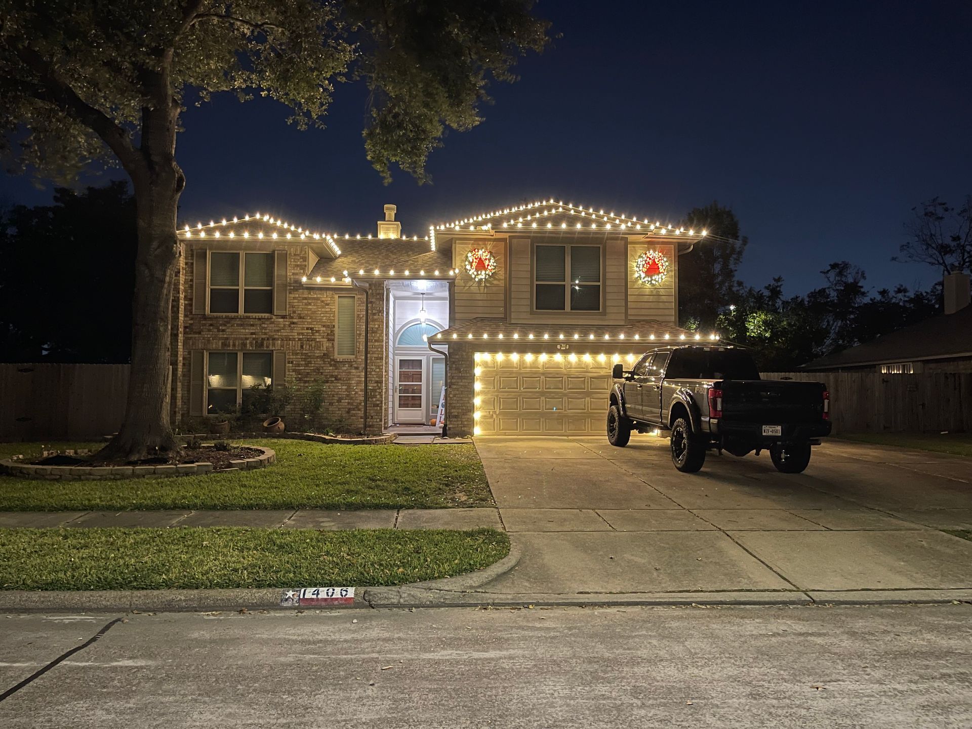 House exterior illuminated by landscape lighting at night, showing brick facade, garage, and landscaping.